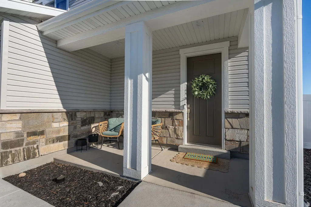 Covered front porch featuring a dark paneled entry door, white trim, stone veneer accents, and light-colored siding