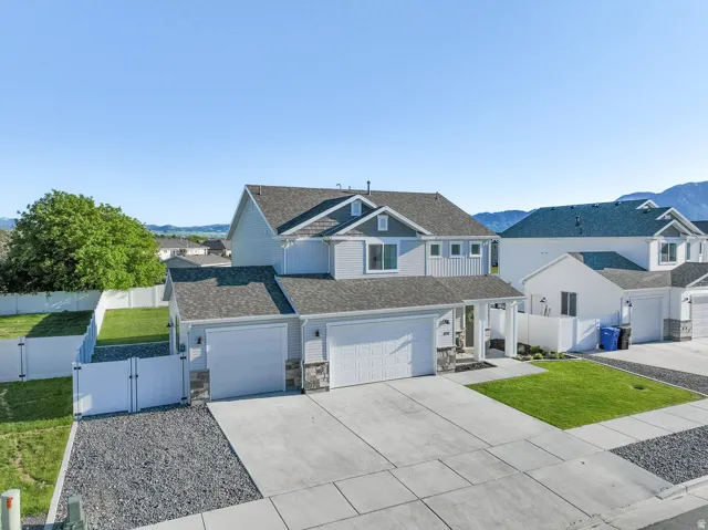 Contemporary residence featuring light grey siding, a dark grey shingled roof, two attached garages with white doors, stone accents, and a concrete driveway