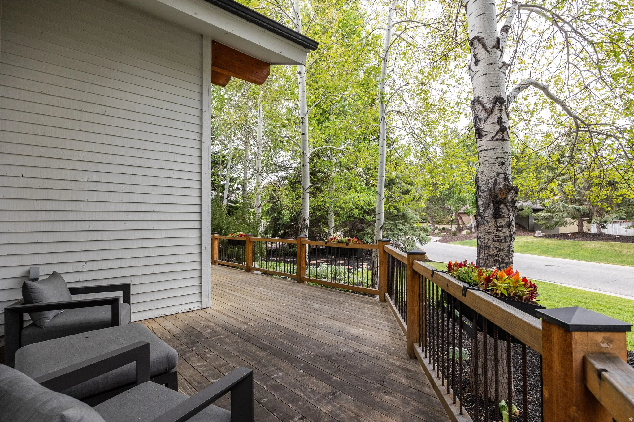 Spacious outdoor deck featuring wood-finish flooring, a horizontal siding exterior, and a wooden railing with black iron balusters
