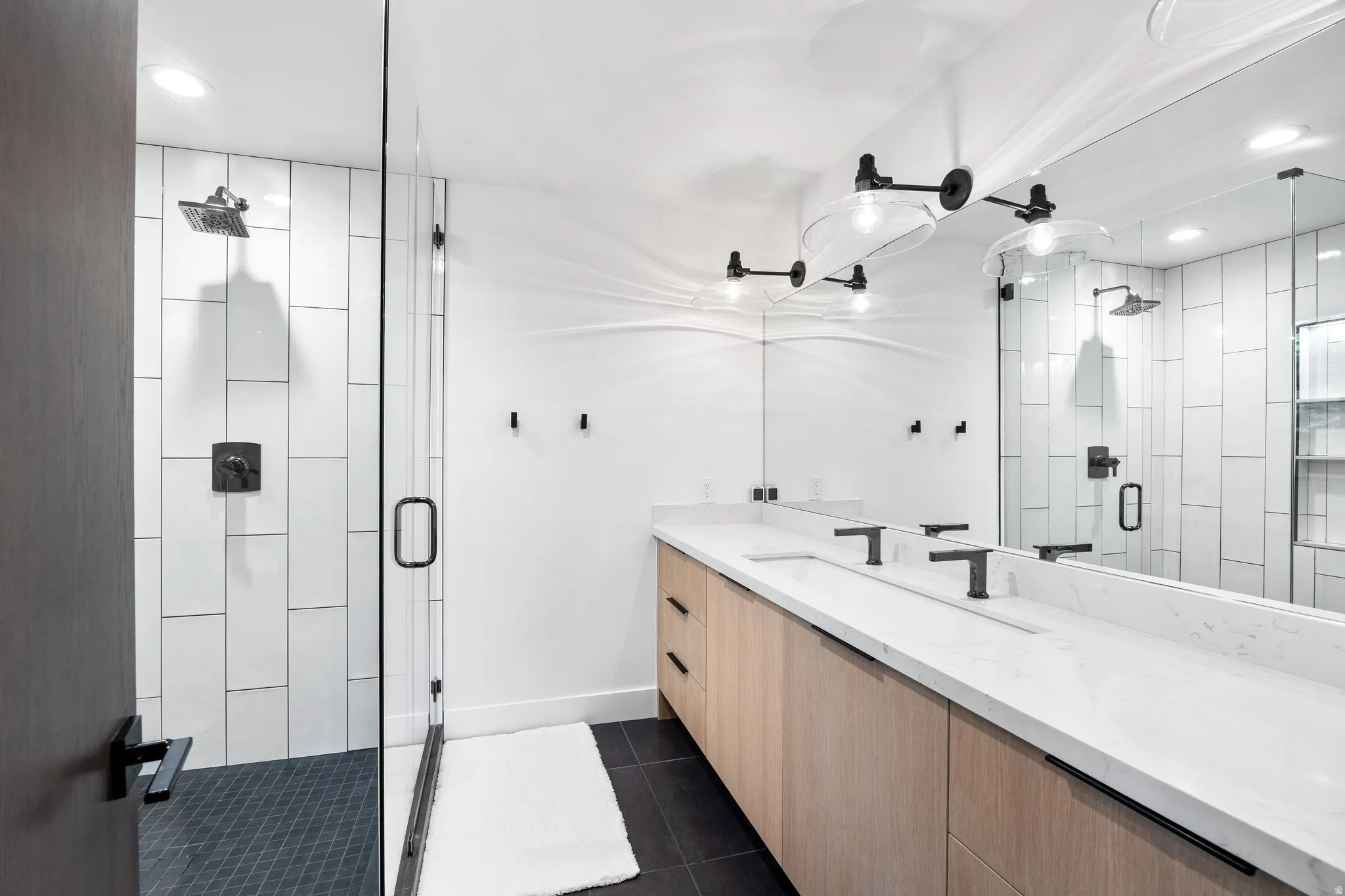 Contemporary bathroom featuring a spacious dual-sink vanity with light wood-finish cabinetry and a white countertop