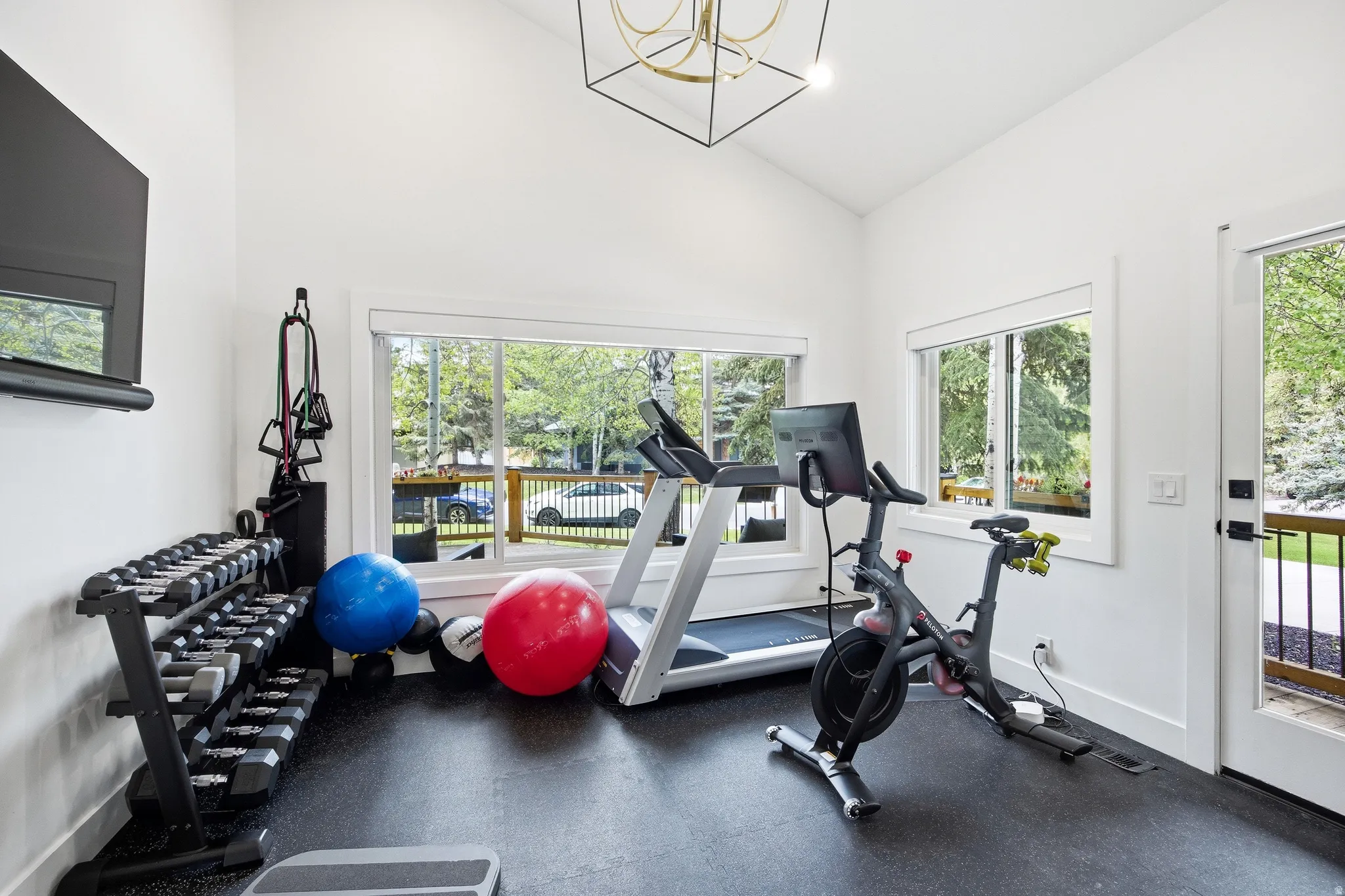 Dedicated fitness room featuring high vaulted ceilings, multiple large windows, and a glass-paneled exterior door