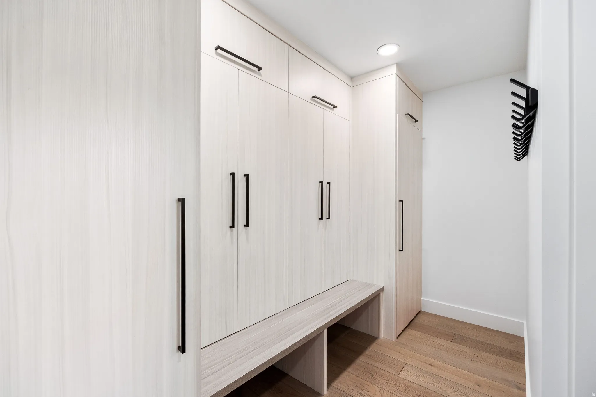 Integrated built-in storage system featuring light wood-finish cabinetry with matte black hardware, recessed lighting, and a coordinating built-in bench