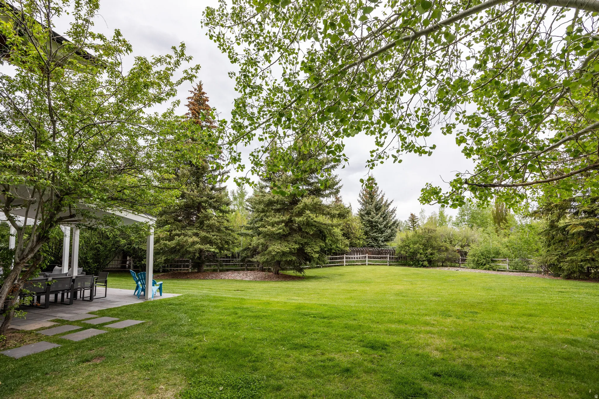 Expansive green lawn surrounded by mature trees, featuring a white perimeter fence