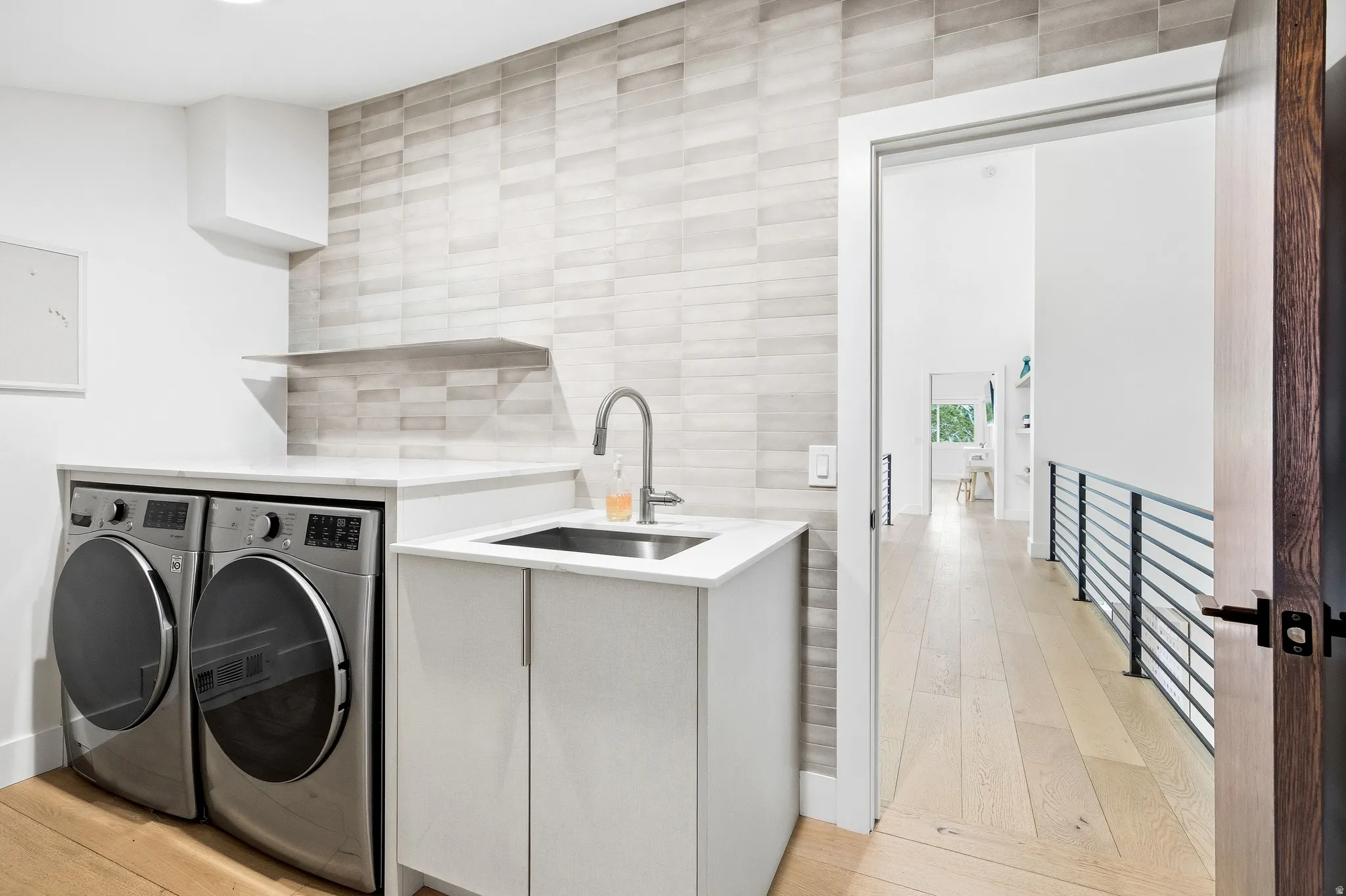 Dedicated laundry space featuring a utility sink with a high-arc faucet, light-toned tiled wall, and open shelving