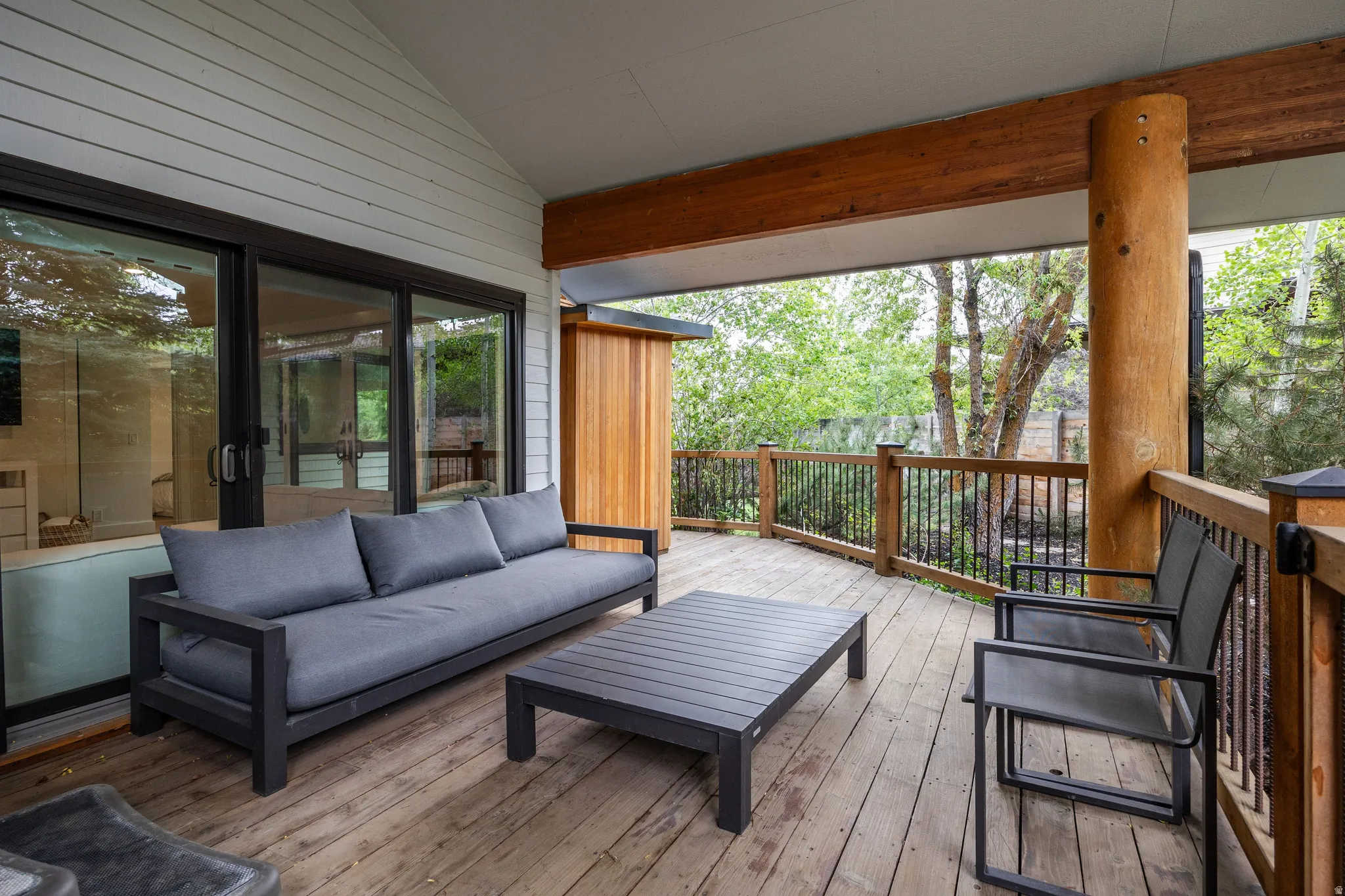 Expansive covered deck featuring wood-finish flooring, a natural wood support pillar, and a black metal railing system