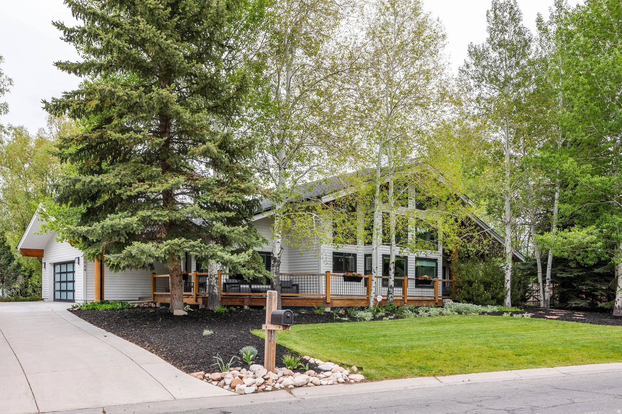 Contemporary residence featuring a white horizontal siding exterior, a wood deck with cable railing, and a black-framed garage door with frosted glass panels