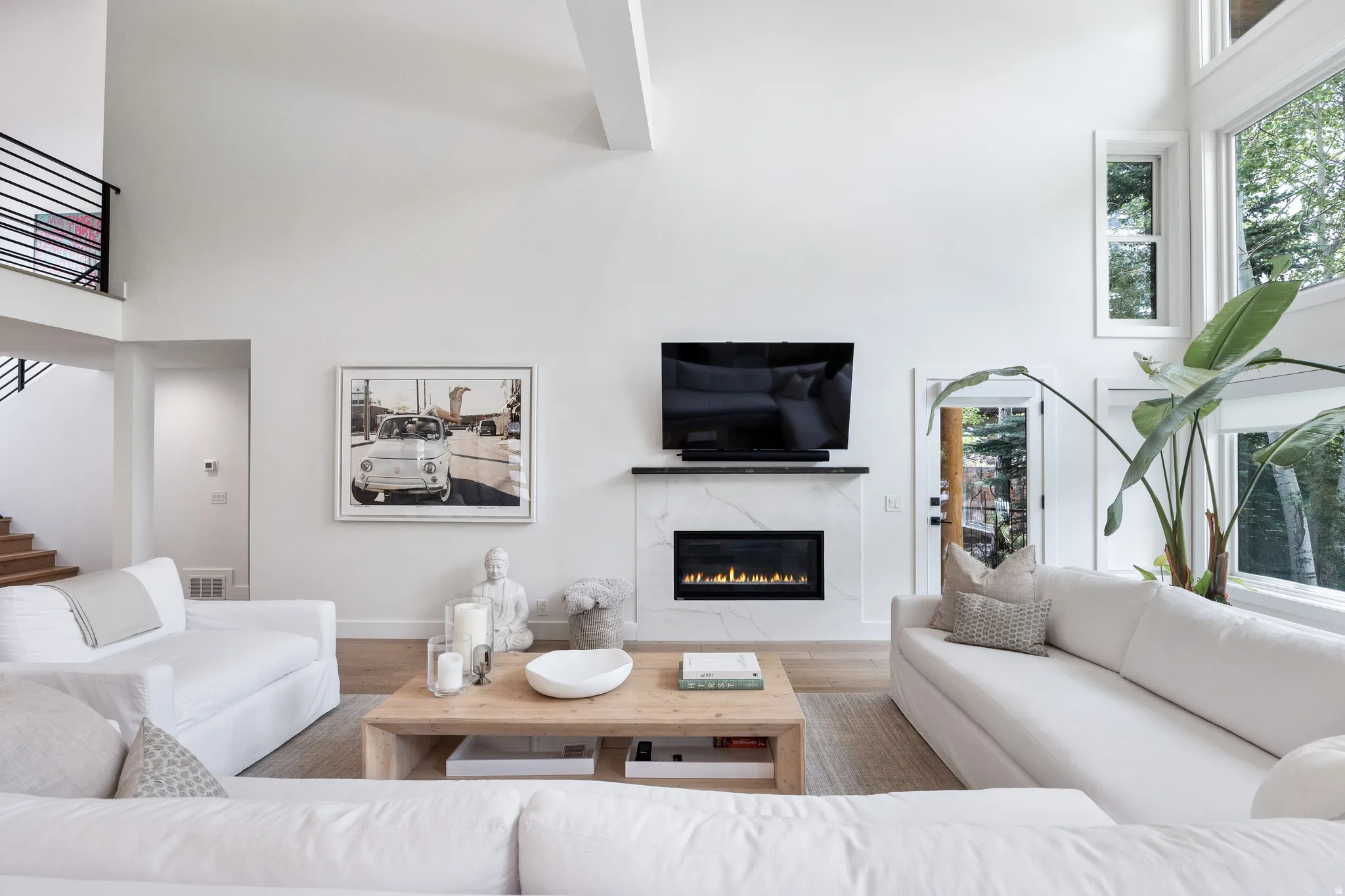 Vaulted living space featuring a modern fireplace with a light-toned surround, hardwood flooring, and abundant natural light from large windows