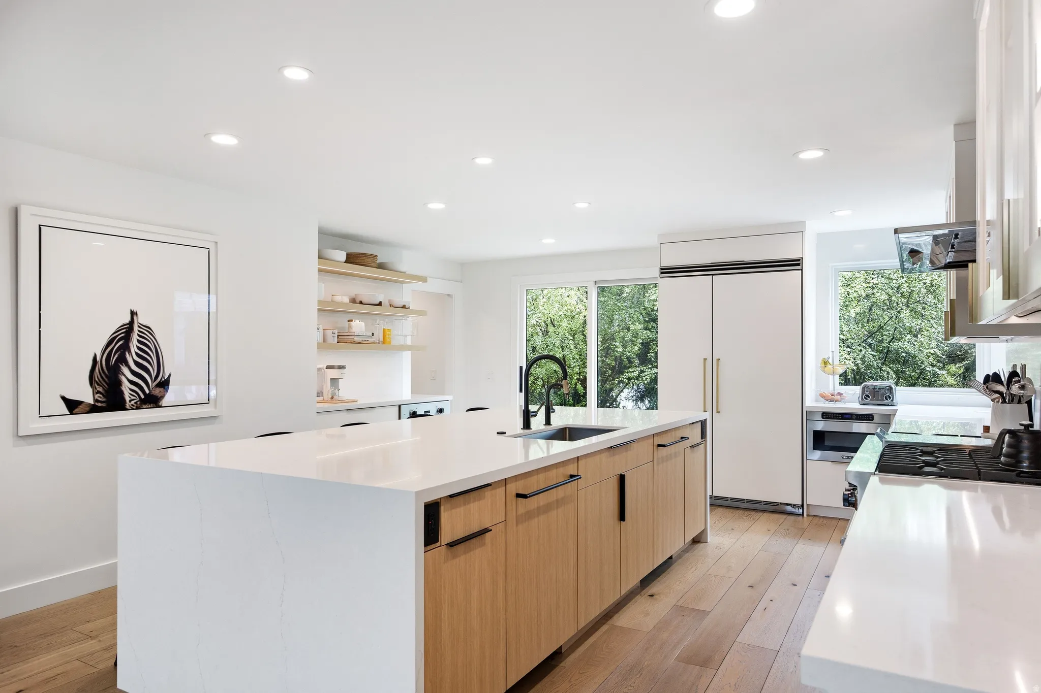 Bright kitchen featuring a substantial island with integrated sink, light wood-finish cabinetry, and white countertops