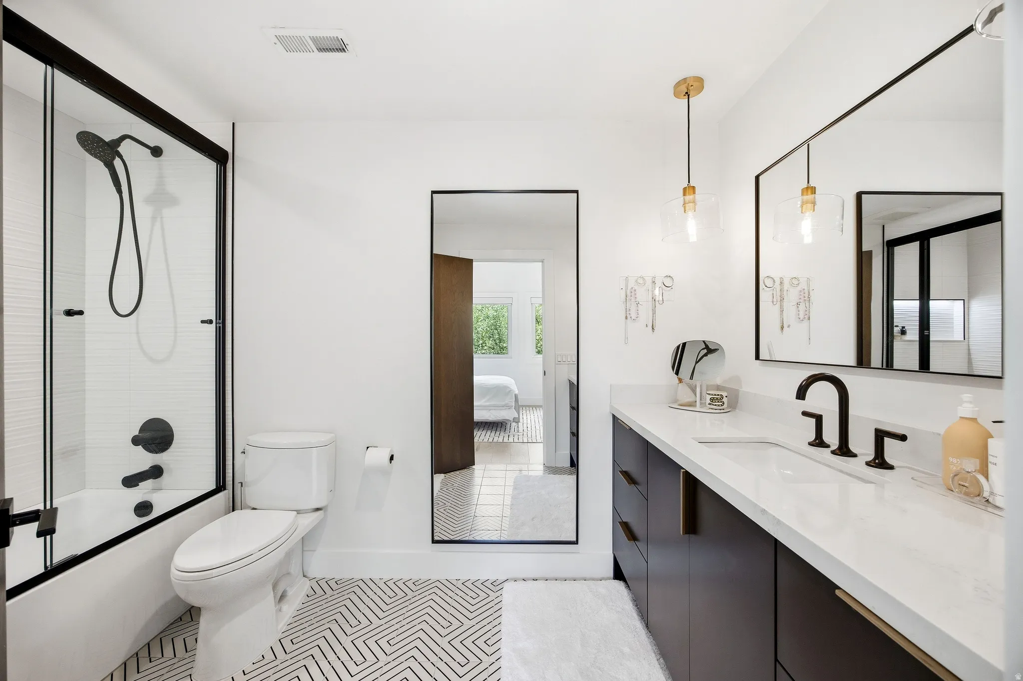 Modern bathroom featuring a single vanity with a white countertop and dark cabinetry, a spacious mirror, and matte black fixtures