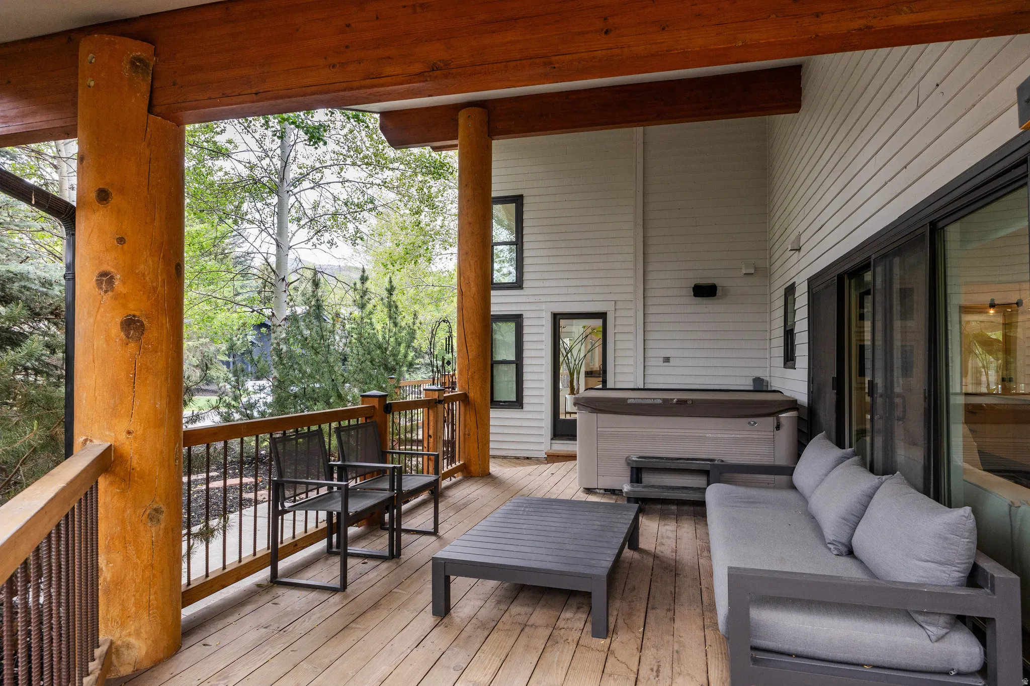 Spacious outdoor deck featuring natural wood-finish flooring, log support beams, and a built-in hot tub