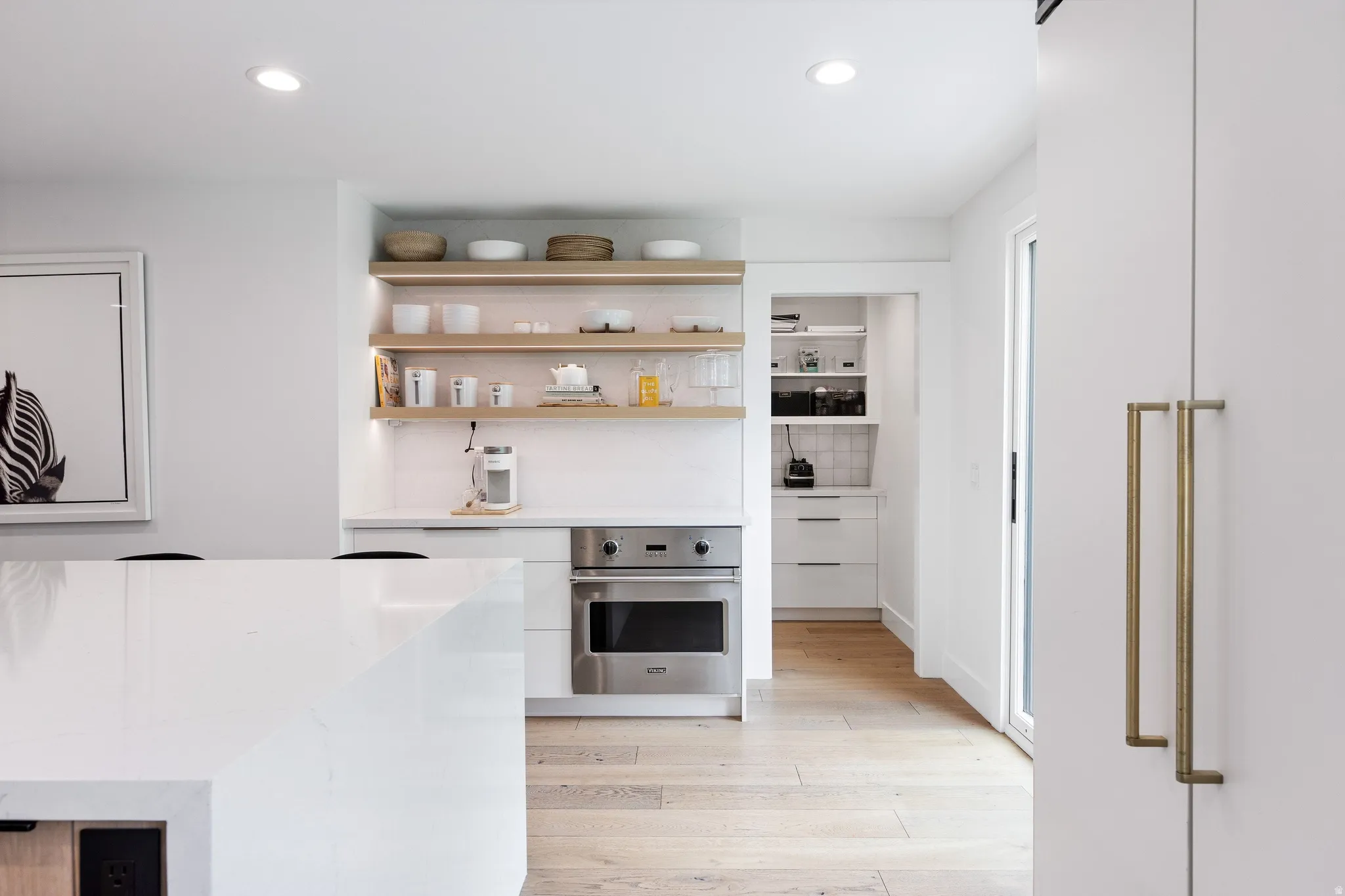 Bright kitchen featuring a white countertop island, stainless steel built-in oven, light wood-finish flooring, and open shelving