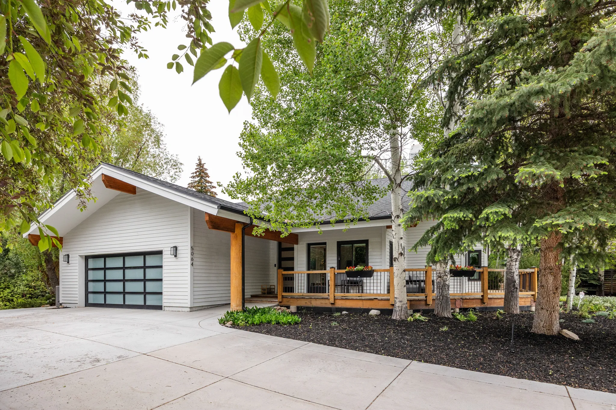 Modern white exterior with a glass-paned garage door, wood beams, and a concrete driveway