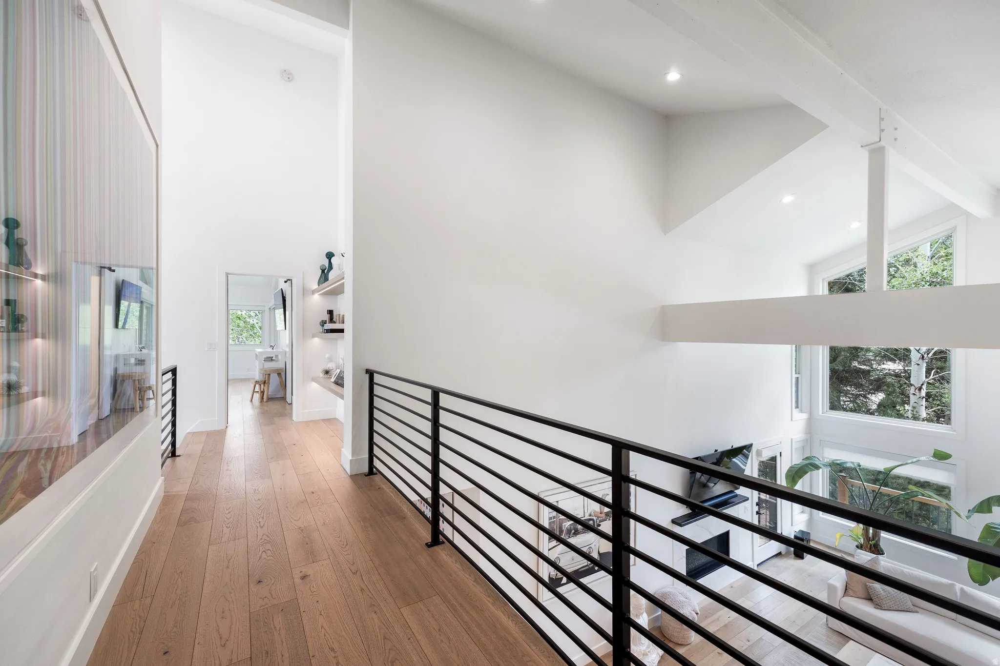 Upper-level hallway featuring light wood-finish flooring and black metal railings overlooking a soaring living space