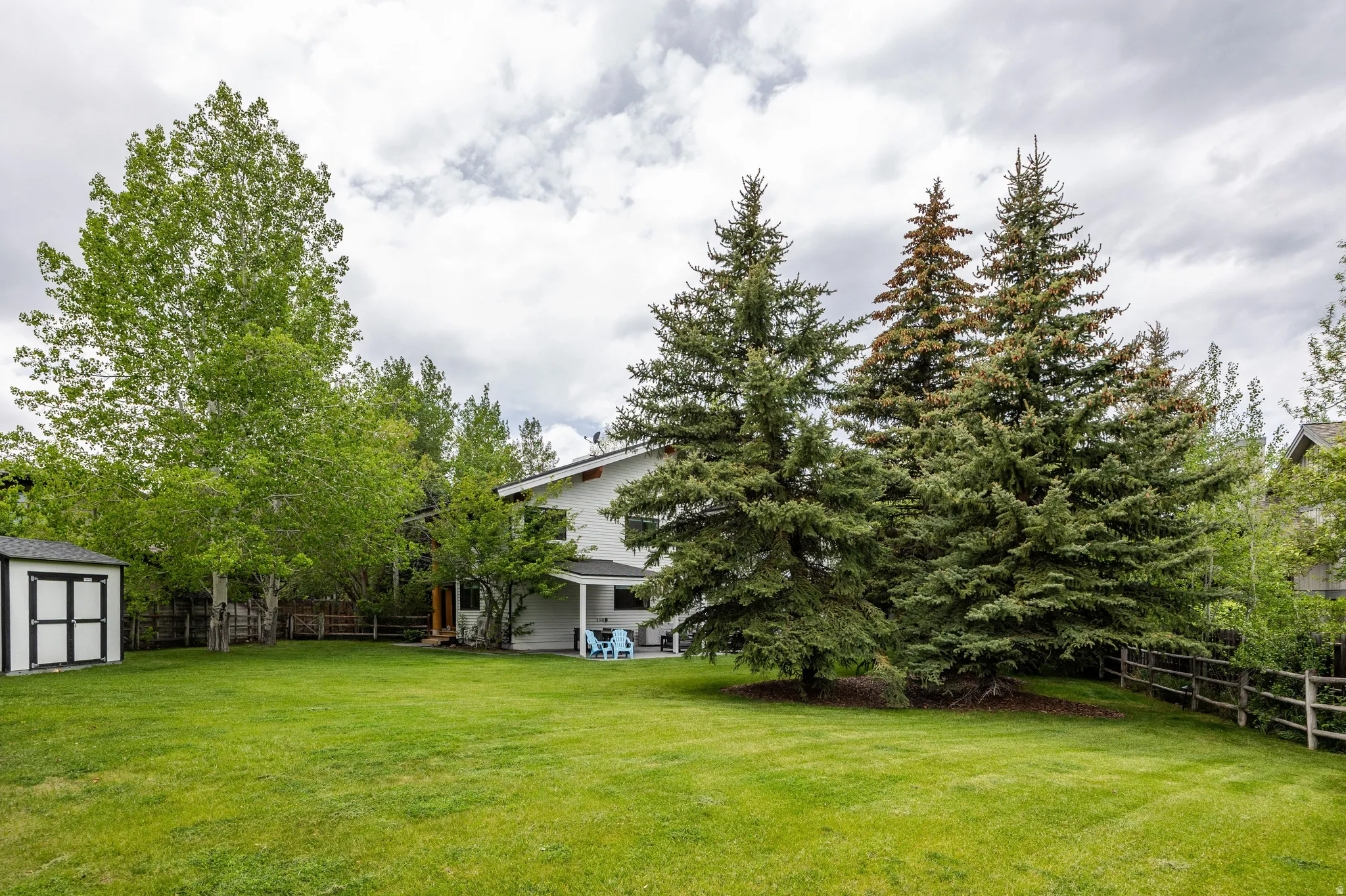 Expansive green lawn with mature trees and a white exterior shed