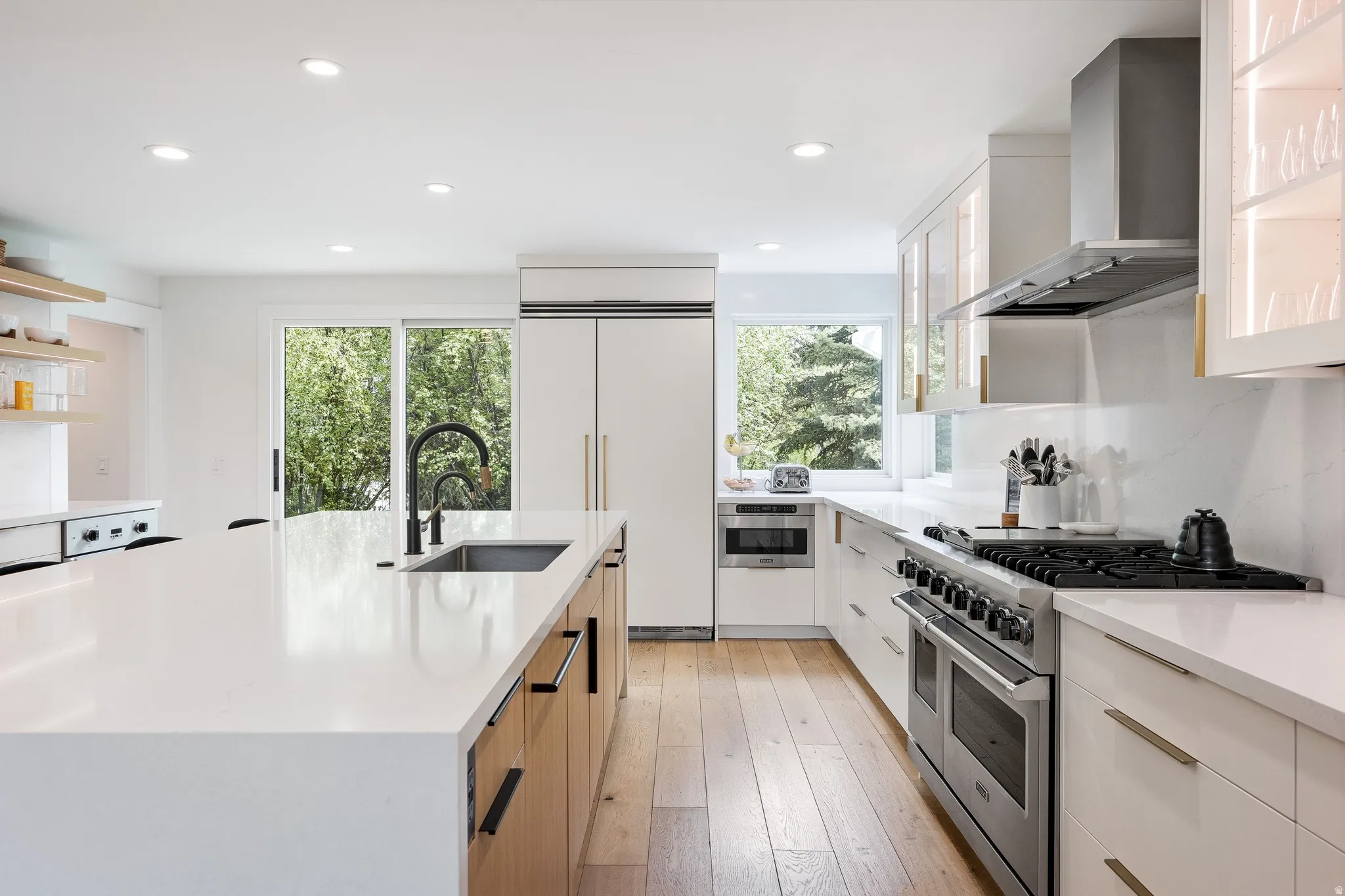 Open-concept kitchen featuring a large island with an undermount sink, stainless steel appliances, wood-finish flooring, recessed lighting, and a sliding glass door
