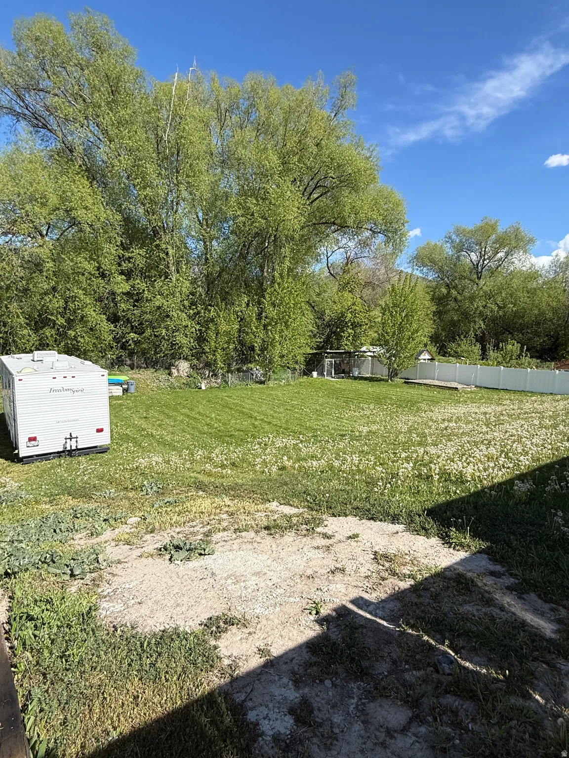 Expansive rear yard featuring green lawn, mature trees, and a white fence boundary