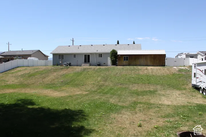 Expansive backyard featuring a sloped lawn and a white vinyl privacy fence