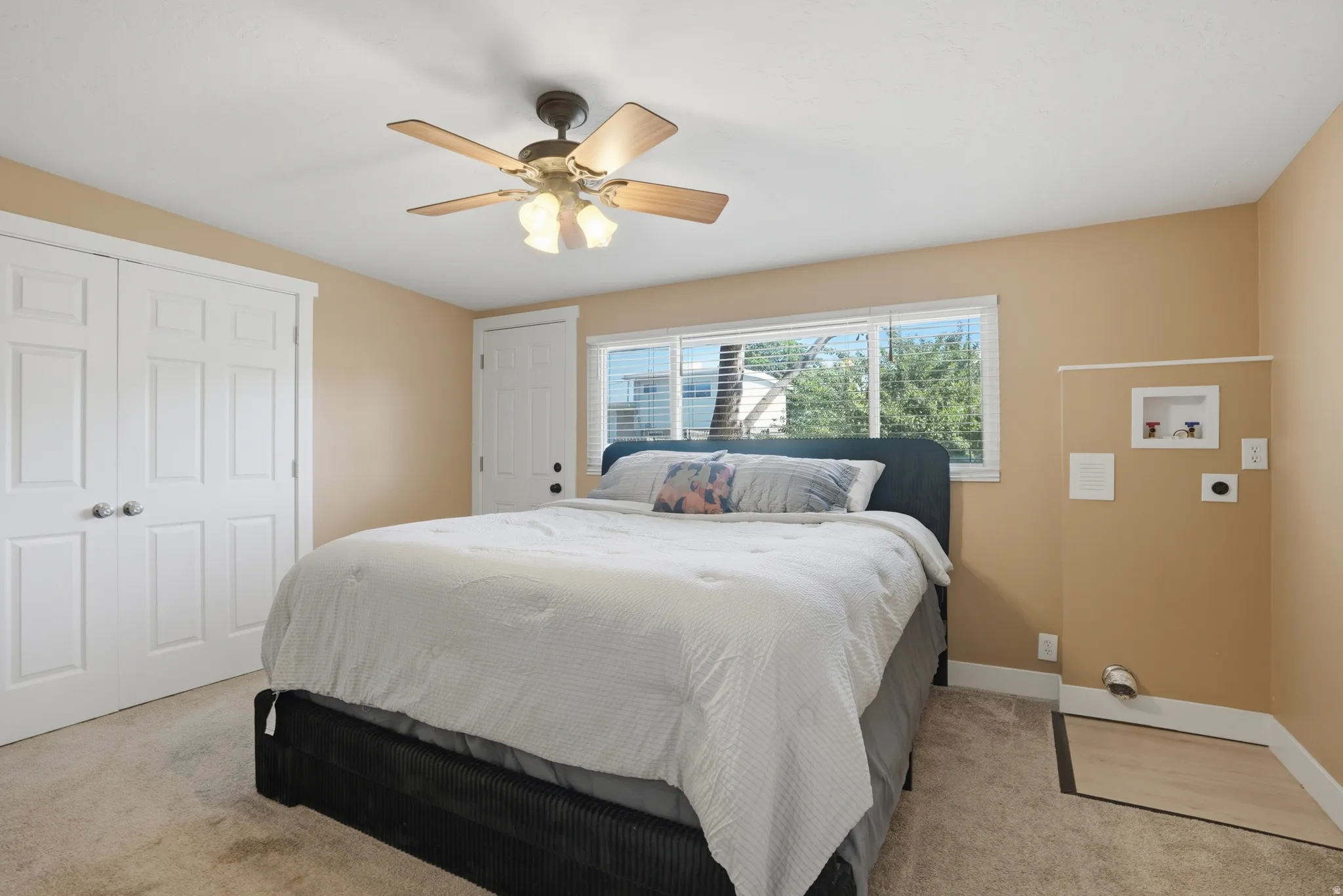 Carpeted room featuring a ceiling fan with light fixture, double-door closet with paneling, a large window, and an exterior access door