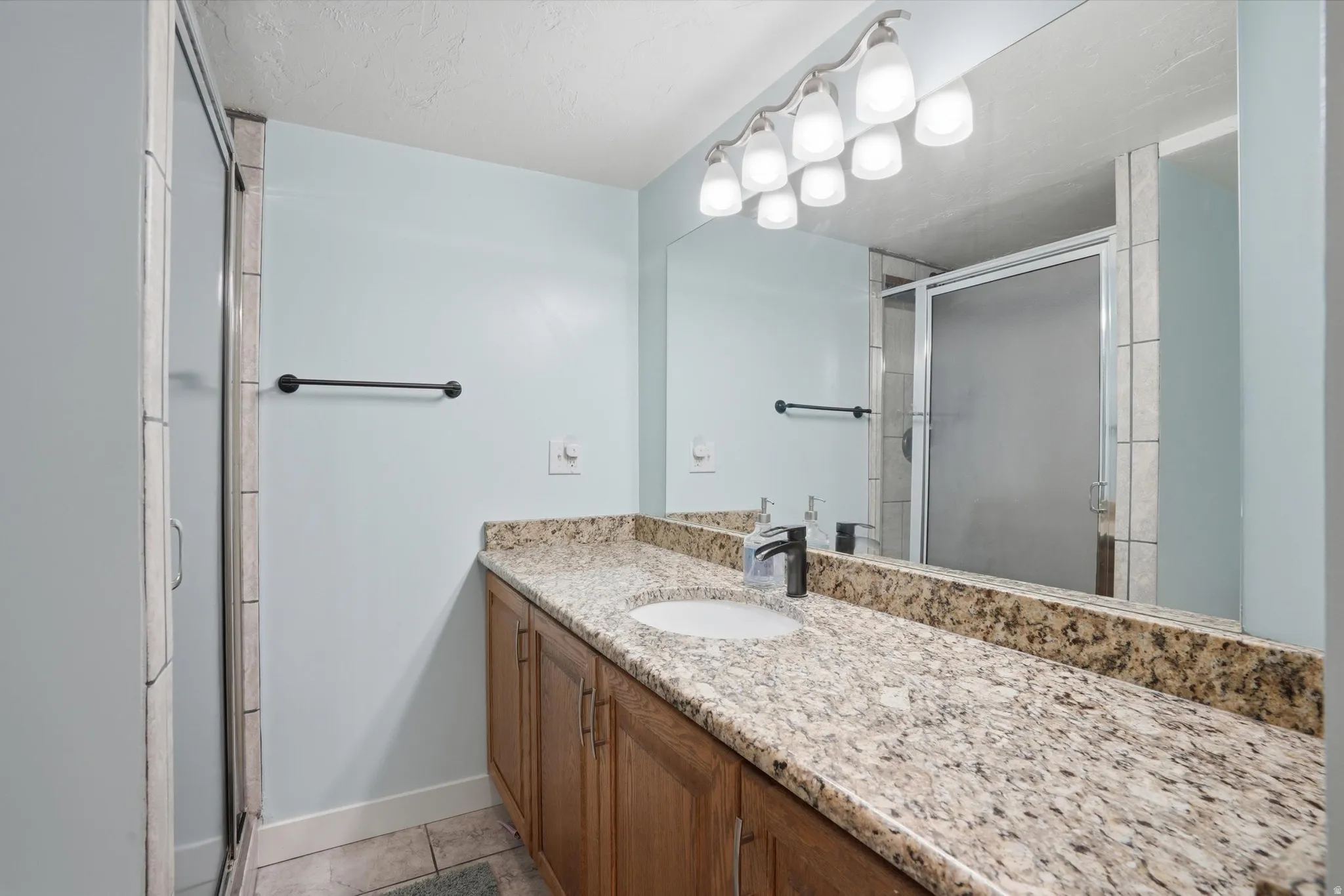 Bathroom featuring a long wood-finish vanity with an integrated sink, speckled stone countertop, and a full-width mirror
