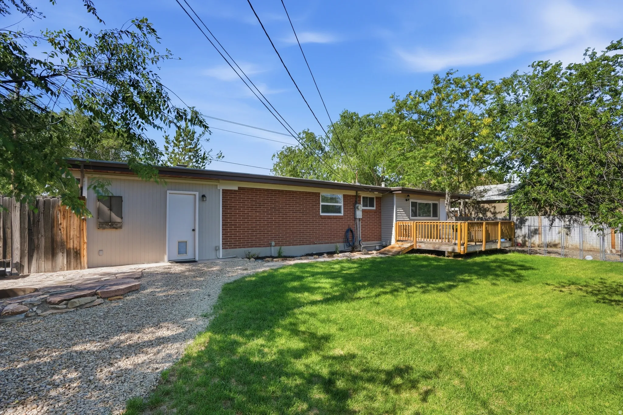 Spacious backyard featuring a large grassy area, a wooden deck with a ramp, and mature trees providing natural screening