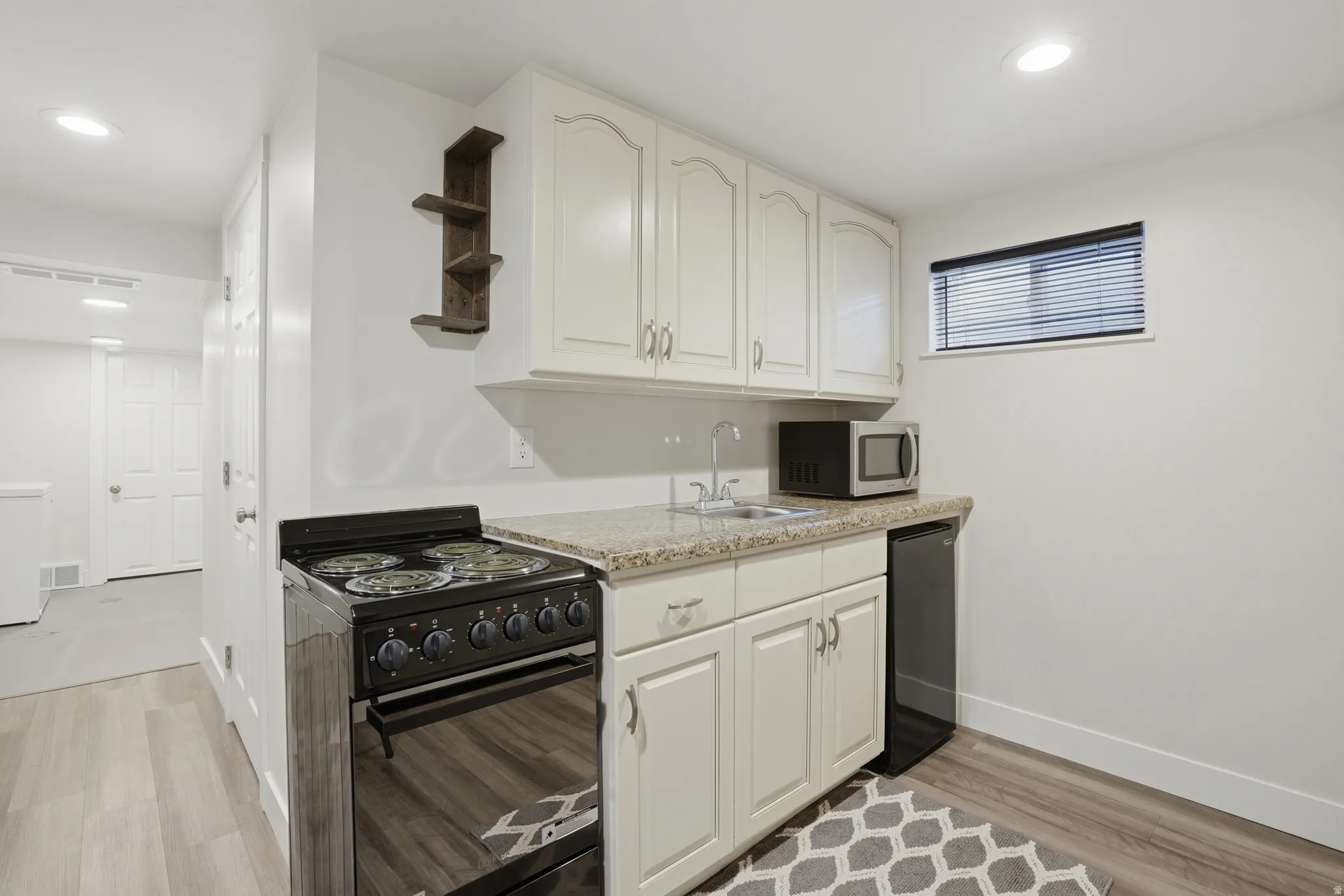 Compact kitchen area featuring a full-size black electric range, light-toned cabinetry, and a speckled countertop