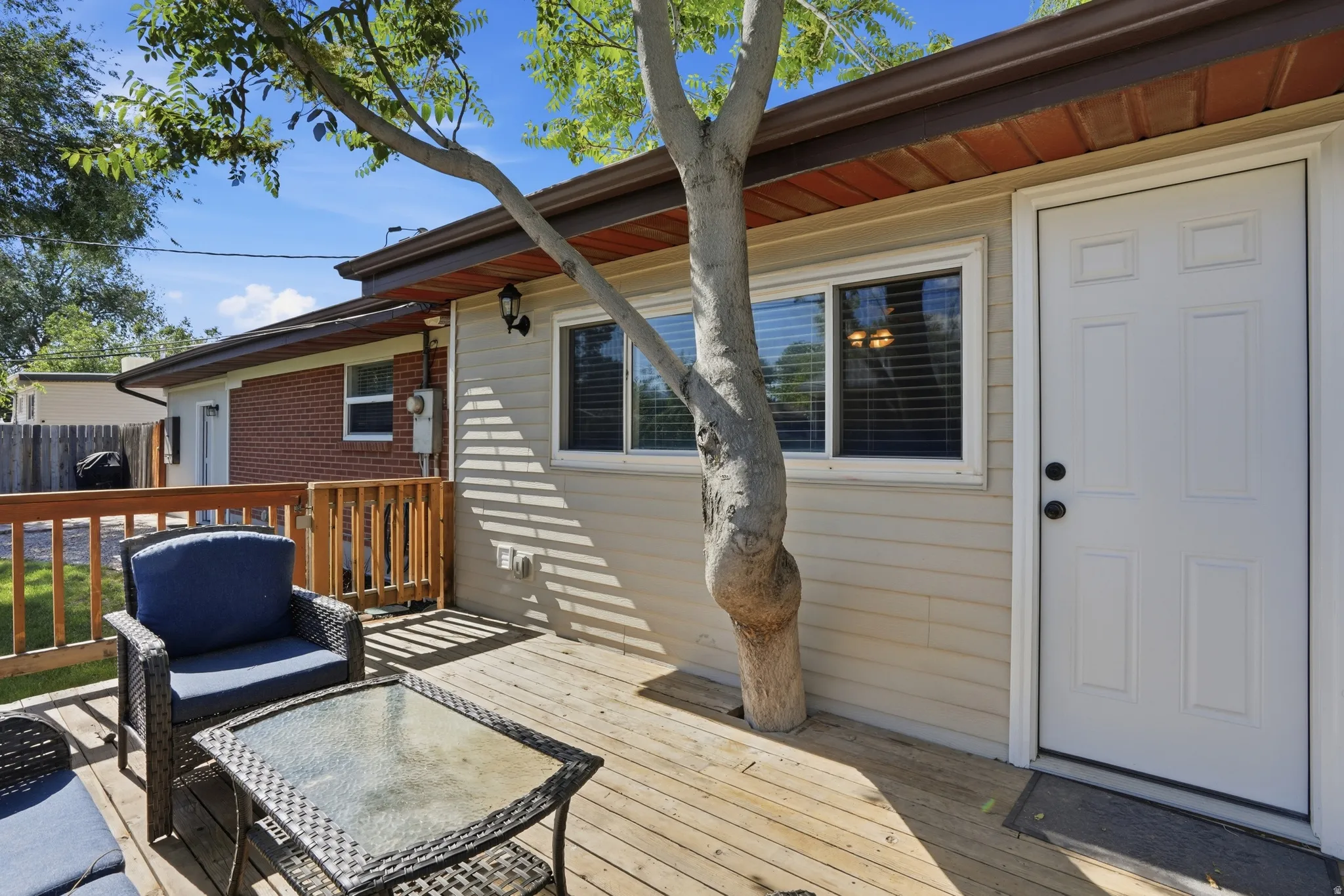 Private wooden deck with full railing, featuring a white paneled exterior door and a large window with blinds