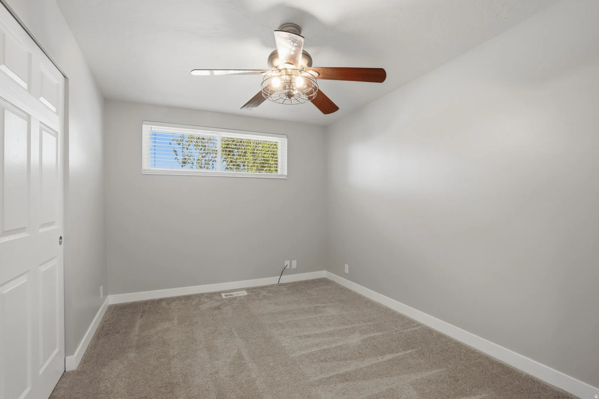 Room featuring neutral gray walls, light-colored carpeting, a horizontal window with blinds, and a ceiling fan with integrated lighting