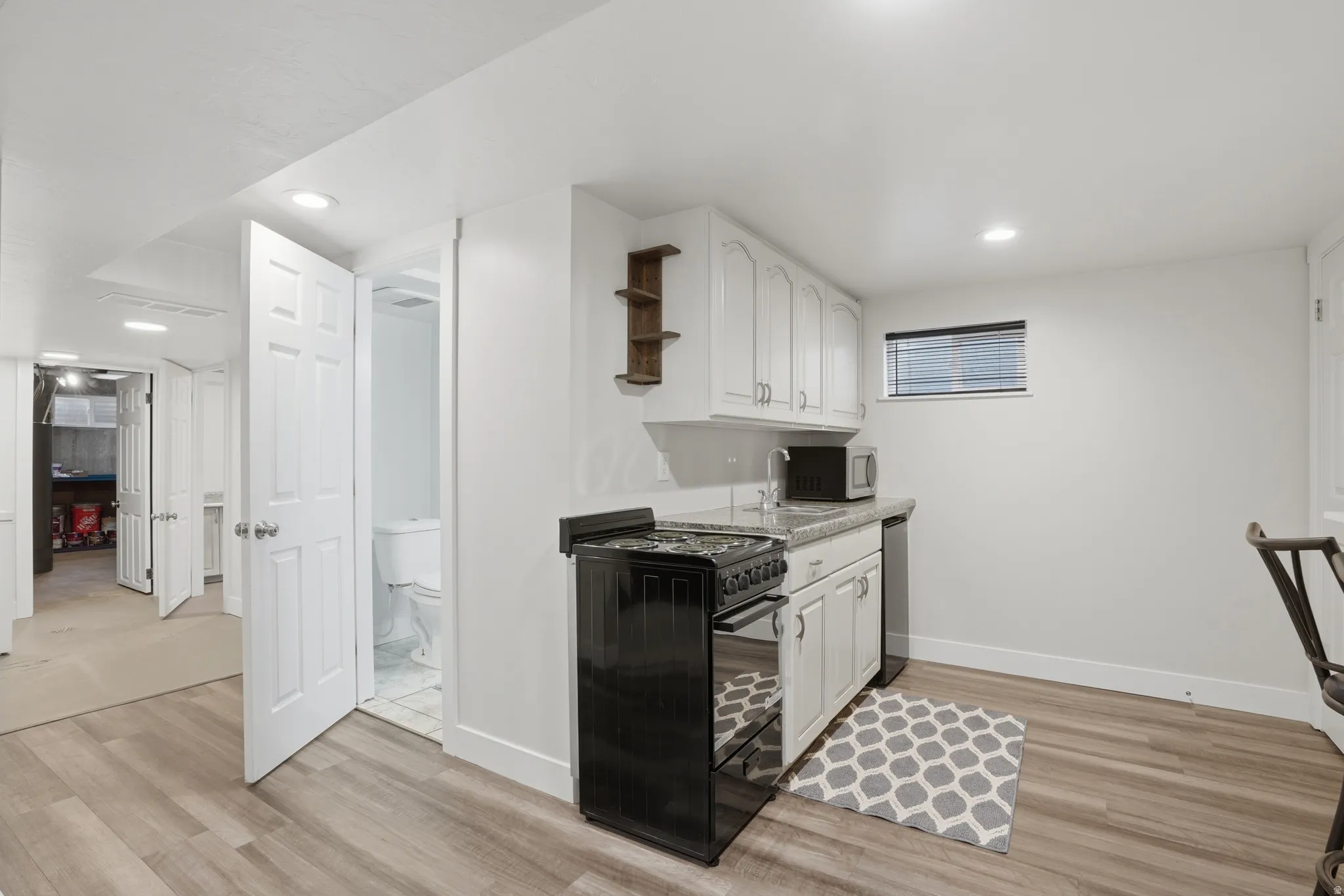 Compact kitchen area featuring wood-finish flooring, white cabinetry, a black range, and a small under-counter refrigerator