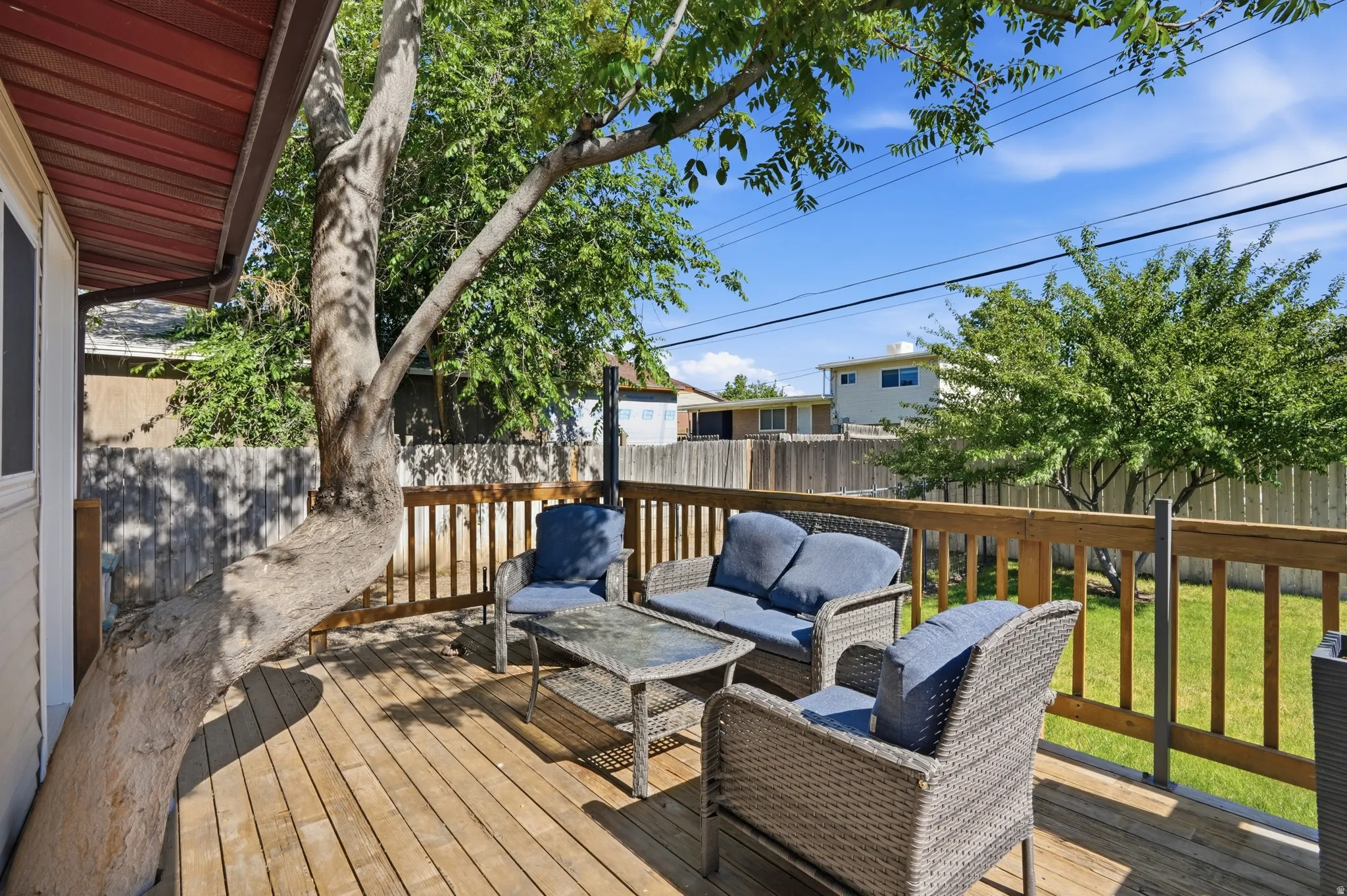 Spacious wood deck with natural wood railing, a mature tree providing natural shade, and a visible wood fence enclosing the yard