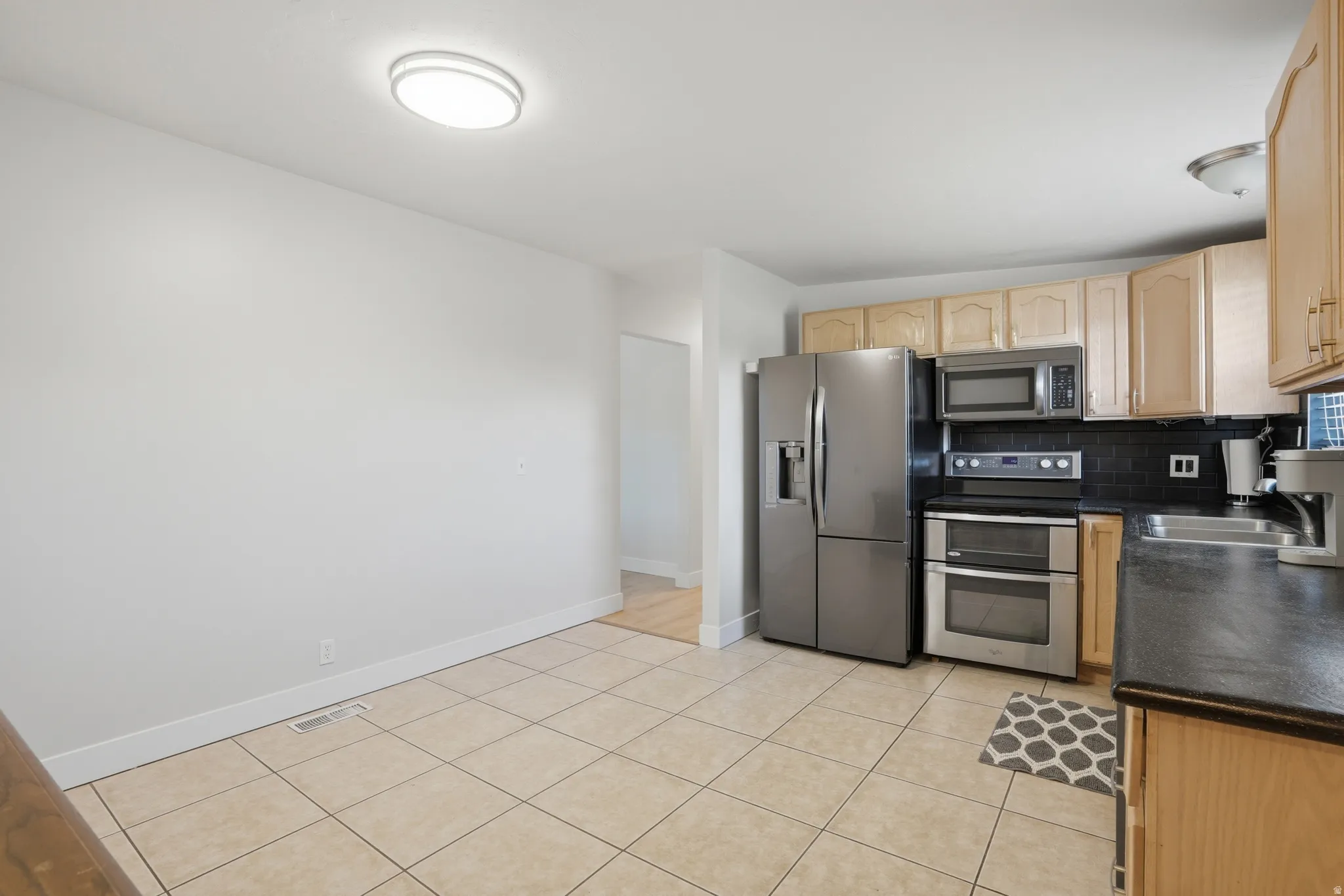 Kitchen area featuring stainless steel appliances, wood cabinetry, dark countertops, and a black subway tile backsplash
