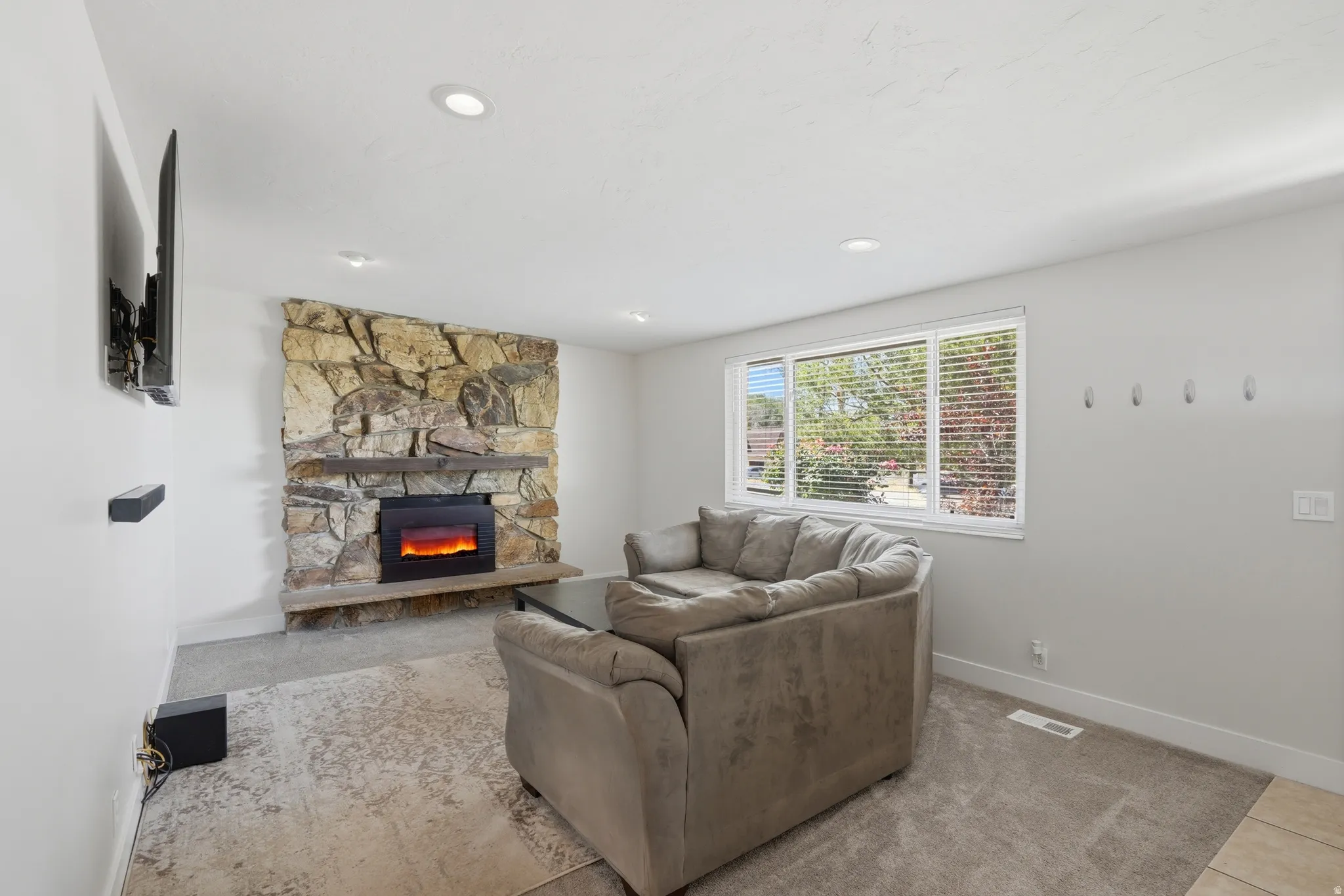 Living area featuring a stone accent wall, an electric fireplace with a wood mantel, recessed lighting, and large windows with blinds