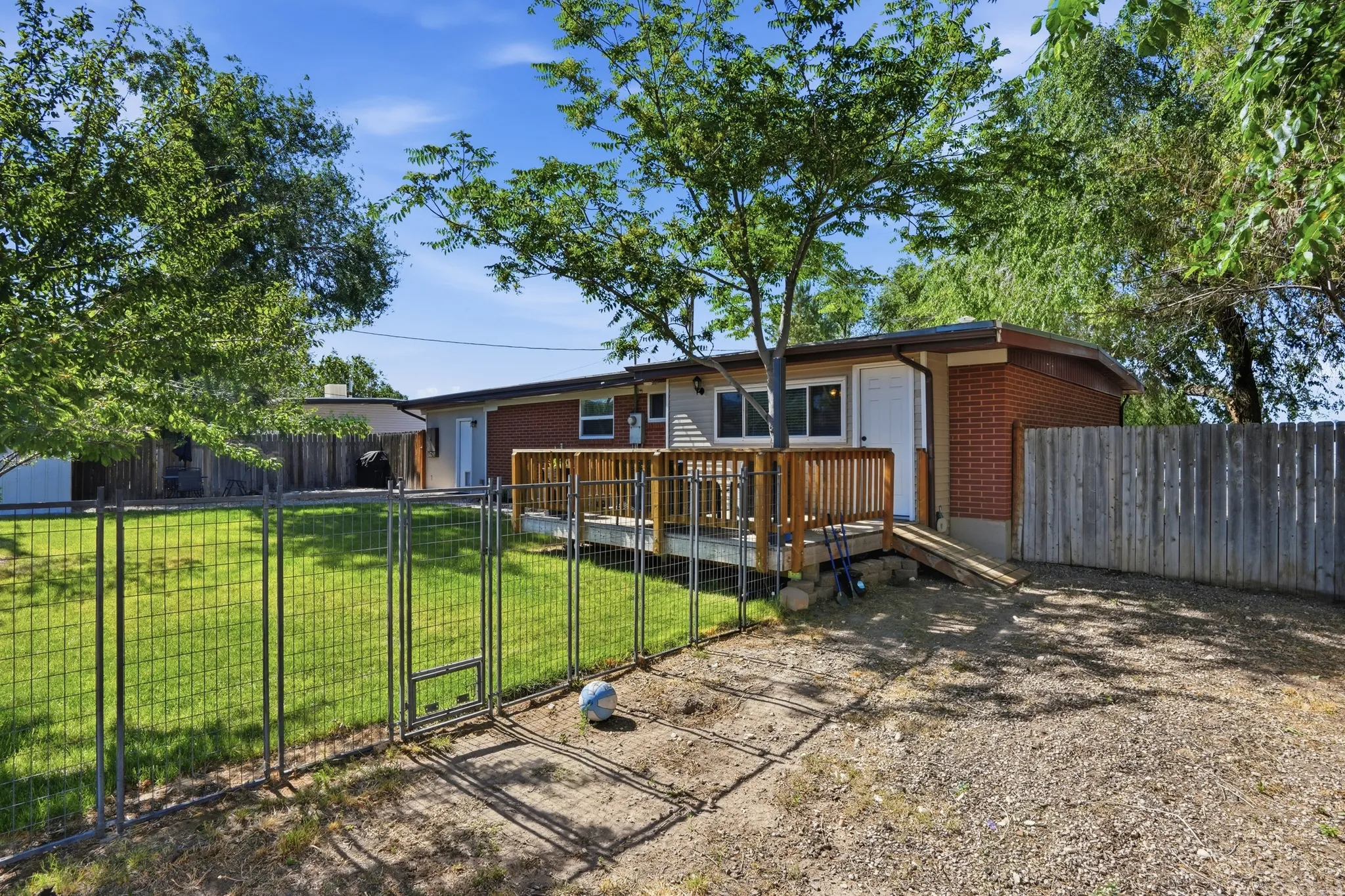 Back exterior featuring a wood deck with railing and ramp access, brick and siding facade, and a metal wire fence enclosing a grassy area