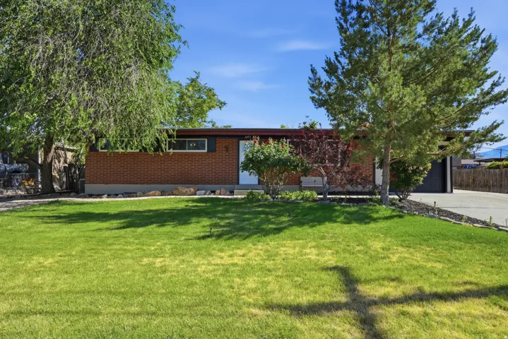 Brick facade residence with a prominent green lawn, mature trees, and an attached garage