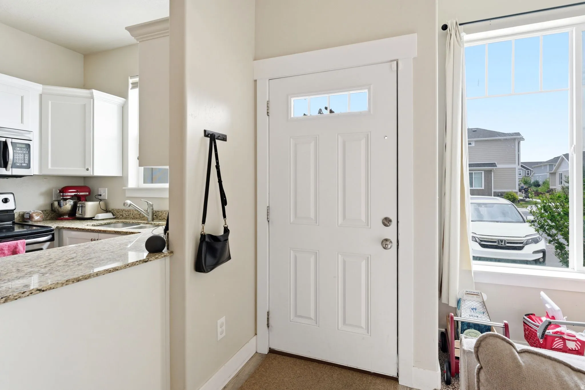 Entryway featuring a paneled door with transom window, wide window framing exterior views, and a half wall with a granite-finish countertop opening to the kitchen