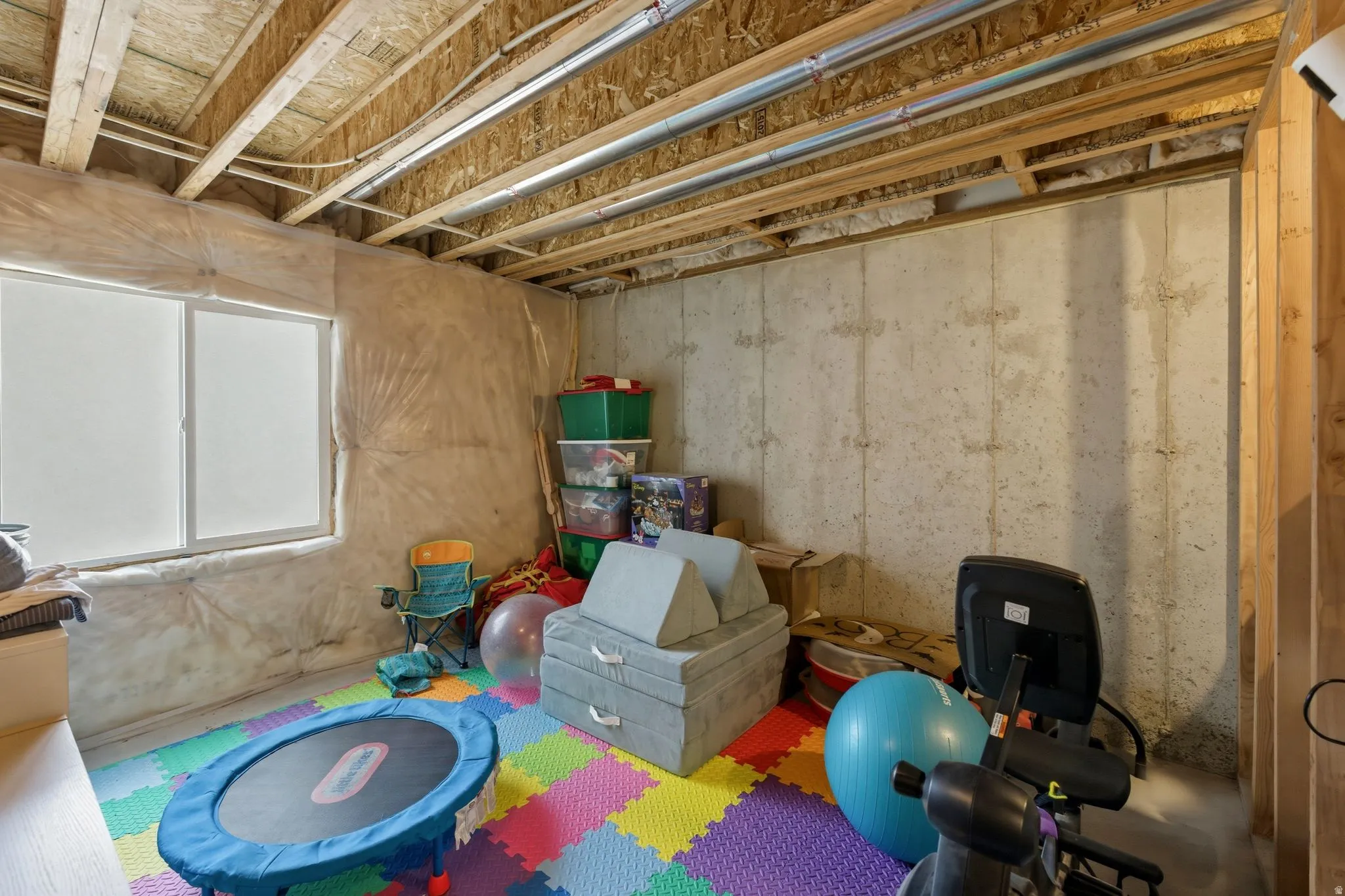 Unfinished basement space featuring exposed wood joists and concrete walls