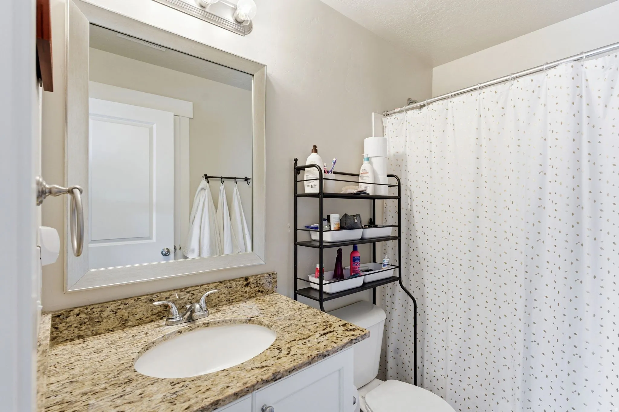 Bathroom featuring a granite countertop with an undermount sink, a framed mirror, and a wall-mounted light fixture