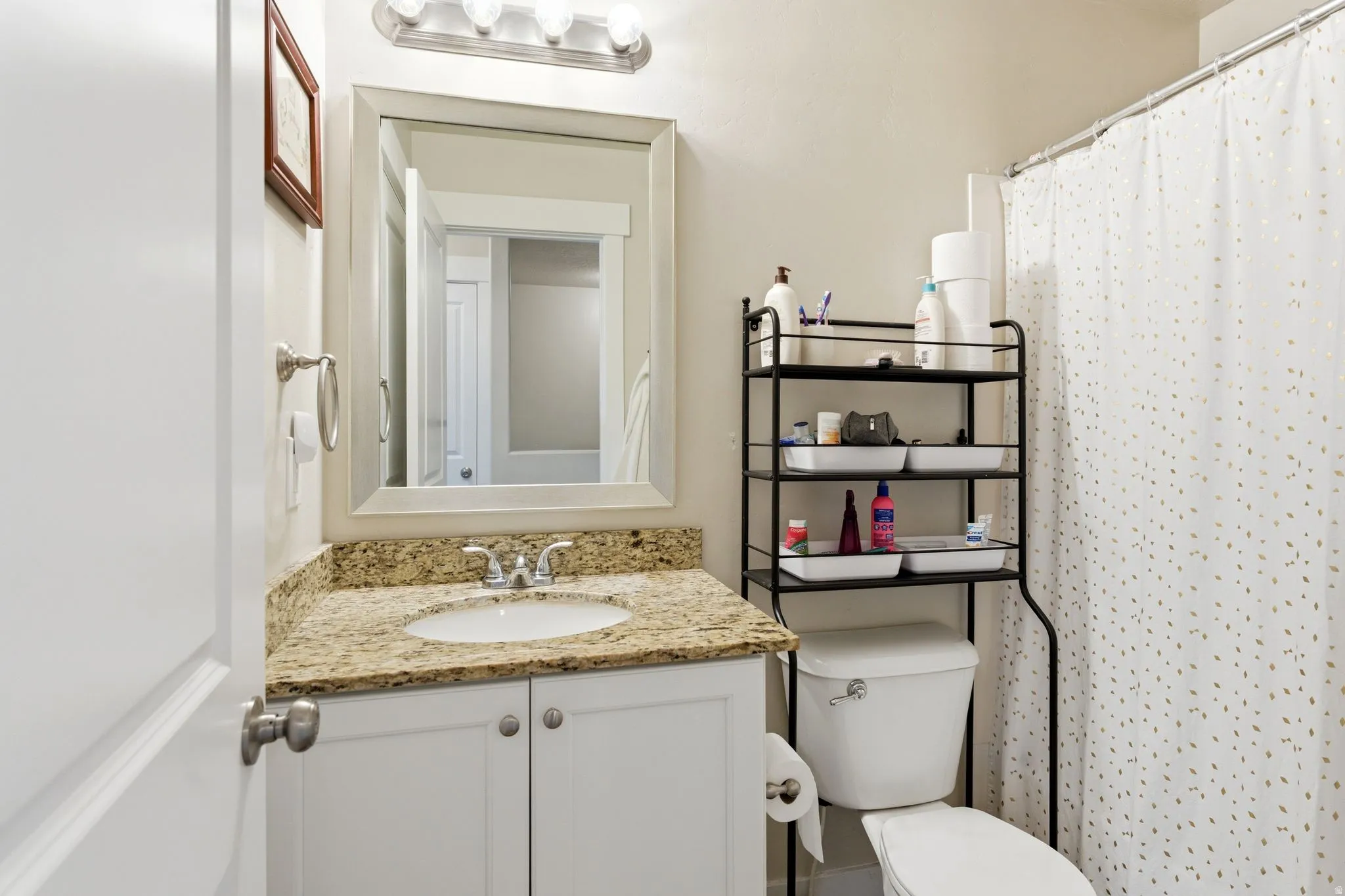 Bathroom featuring a vanity with a granite-finish countertop, undermount sink, and polished chrome faucet