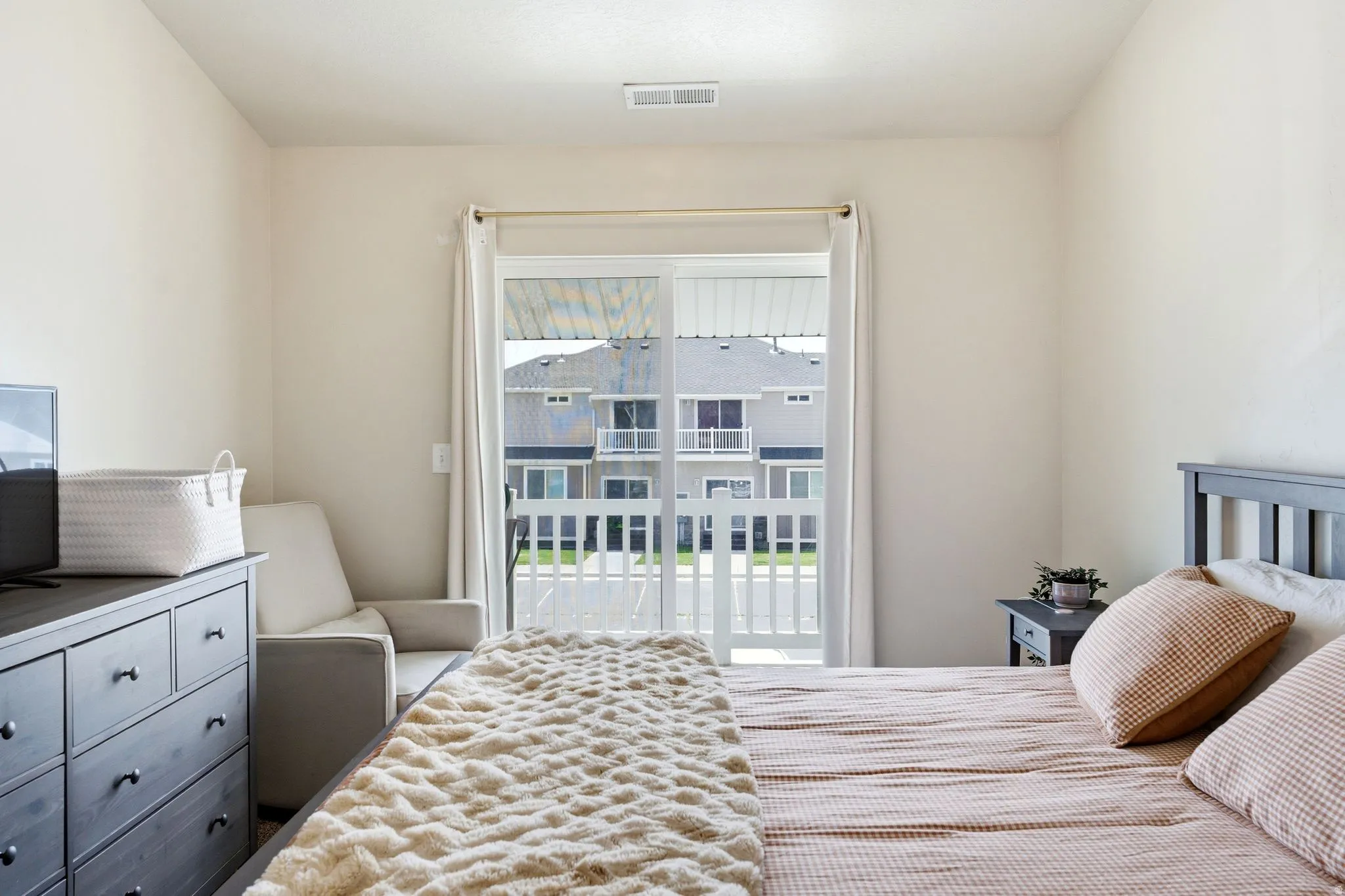 Bedroom featuring a sliding glass door to a private balcony with white railings, light-colored walls, and a built-in ceiling vent