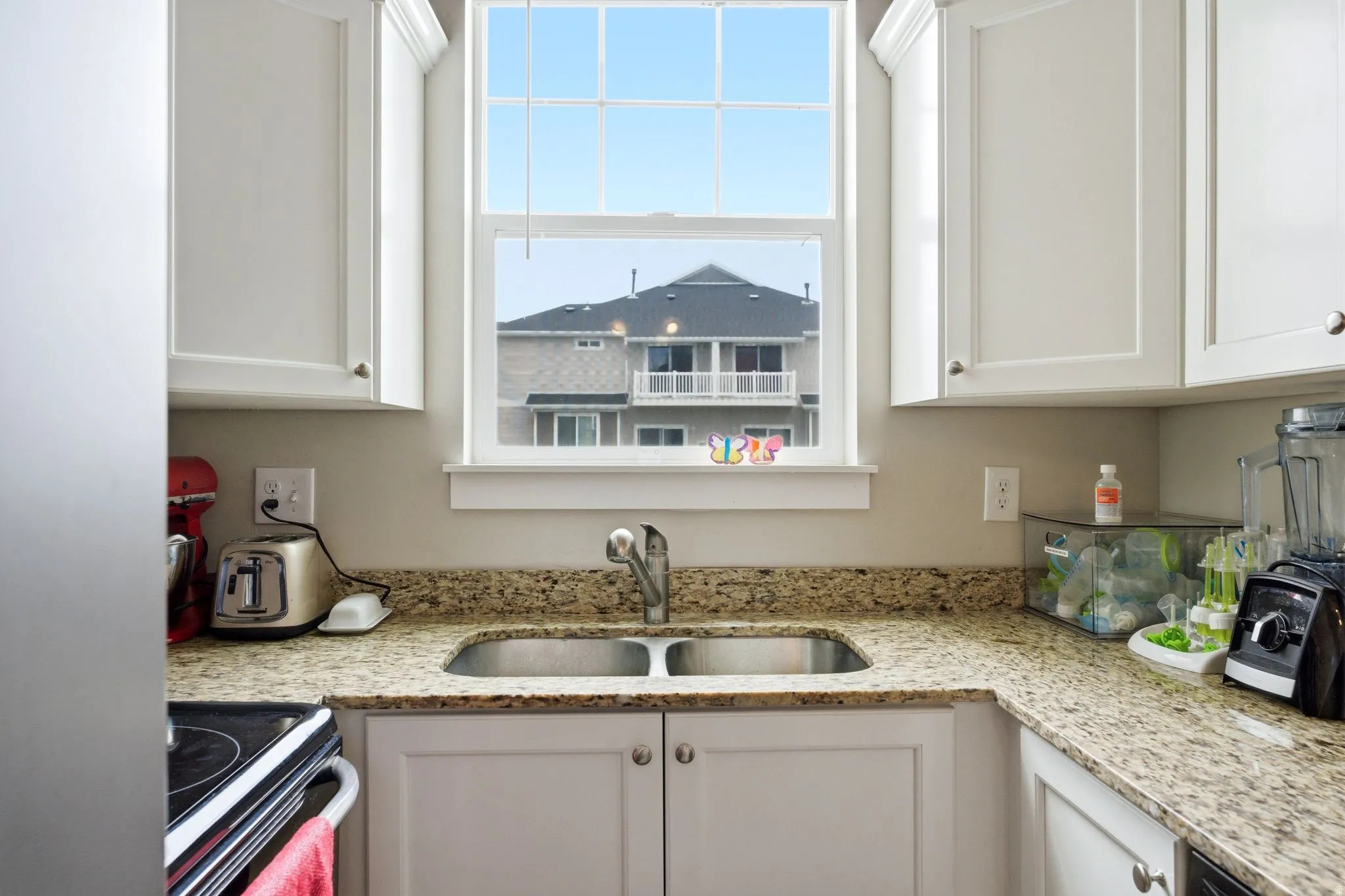 Kitchen featuring a double basin stainless steel sink, granite countertops, white cabinetry with silver hardware, and a window with white trim