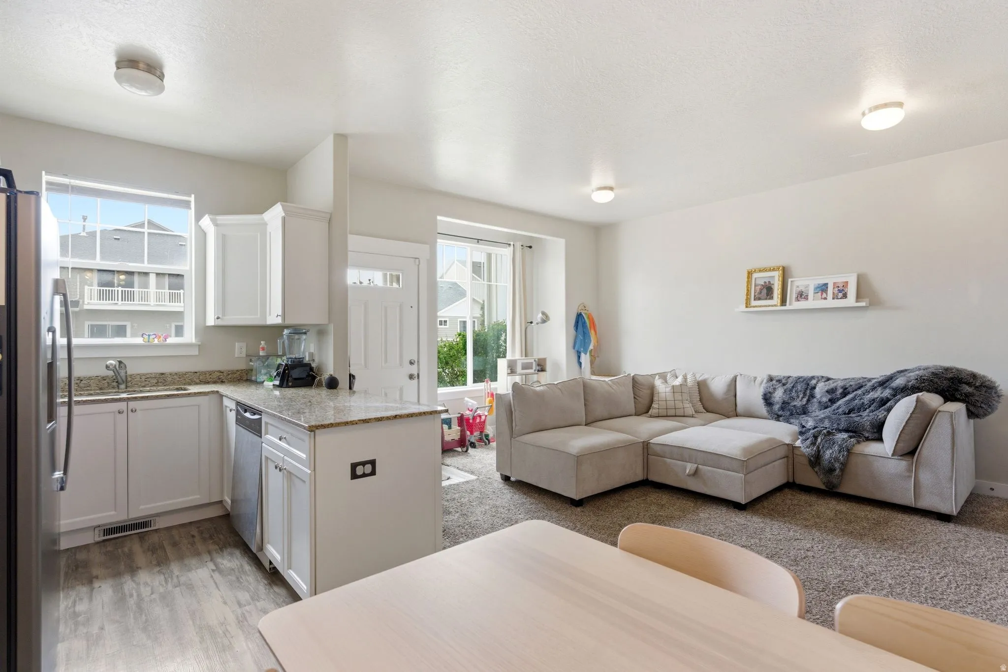 Open-concept living area with a white kitchen featuring stainless steel appliances, a corner sink, and a multi-tone countertop