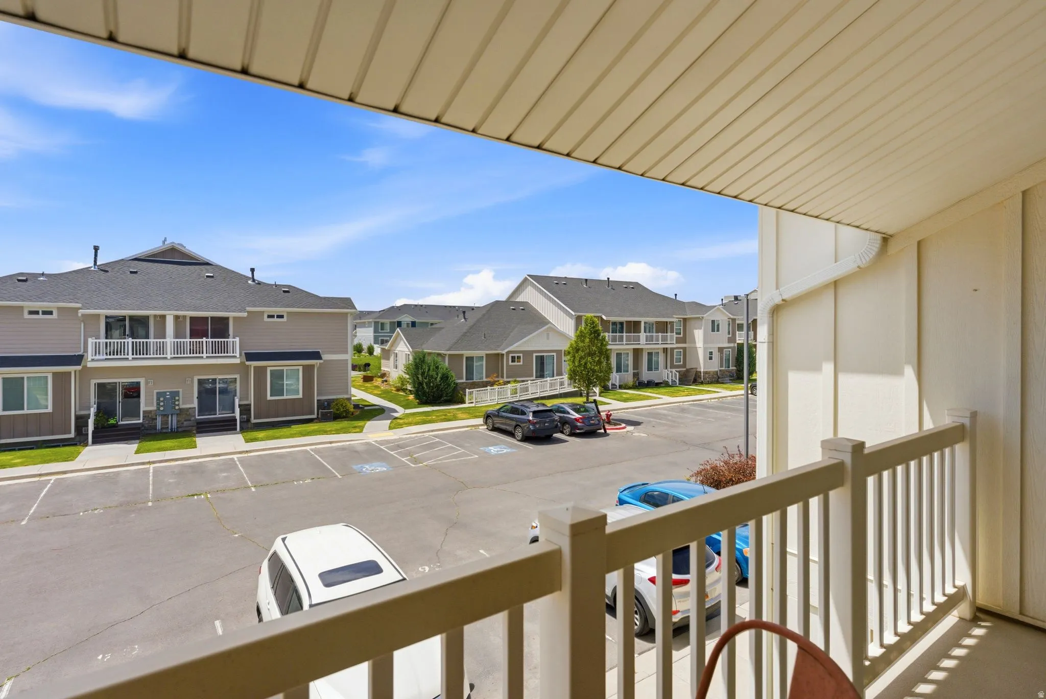 Outdoor balcony with a cream-colored railing and soffit, overlooking a community with multi-level residential buildings