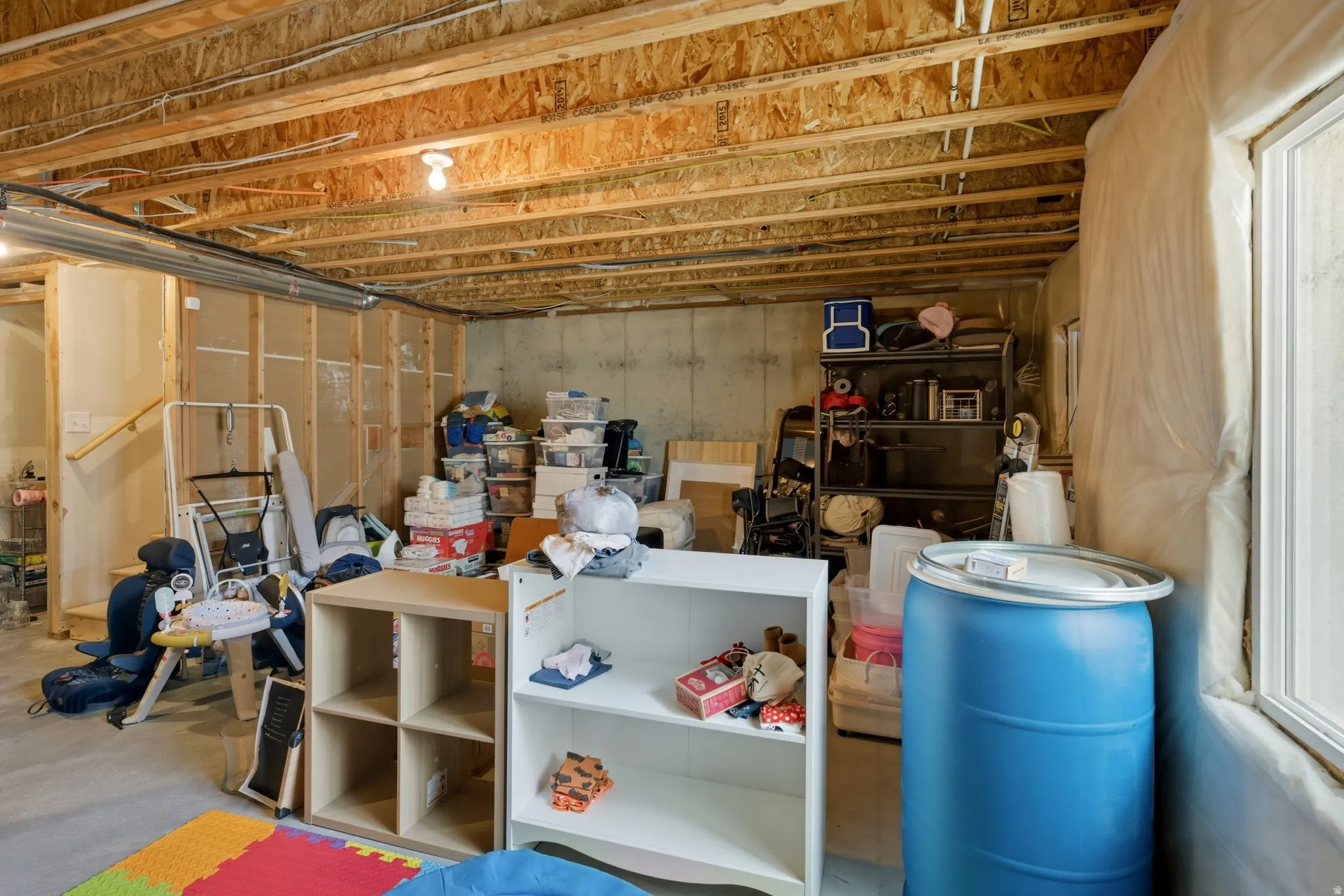 Unfinished basement space with exposed ceiling joists and concrete walls, featuring a window and partial framing