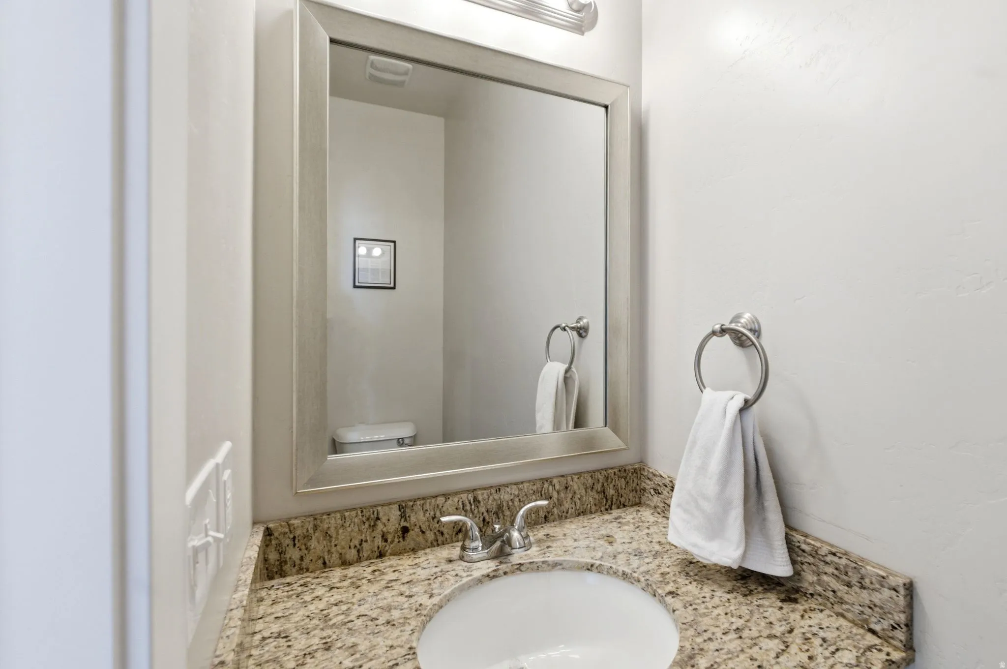 Contemporary vanity featuring a built-in basin sink, granite countertop, and a framed mirror with a mounted light fixture