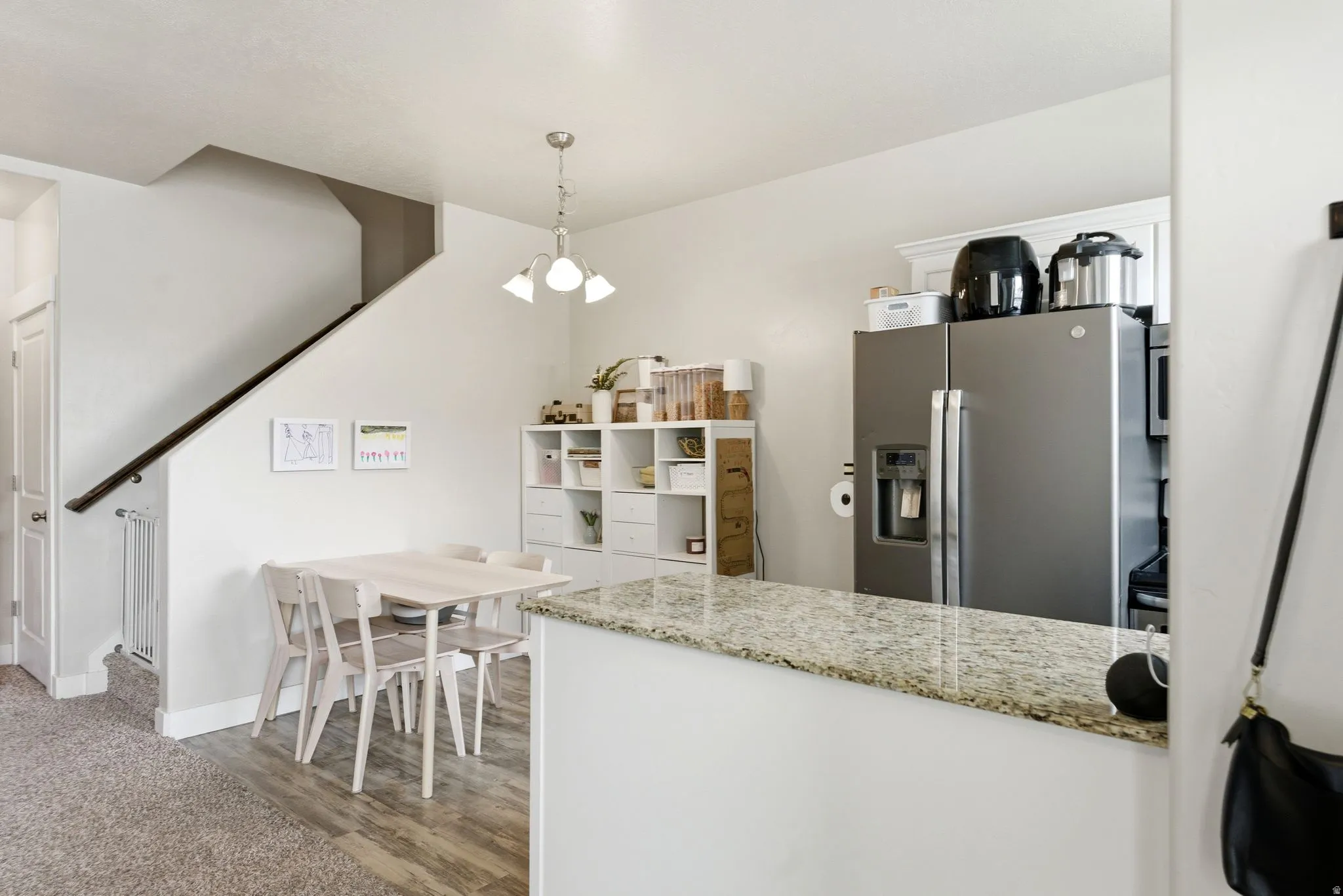 Open-concept kitchen and dining area featuring a granite countertop peninsula, stainless steel refrigerator, and wood-finish flooring