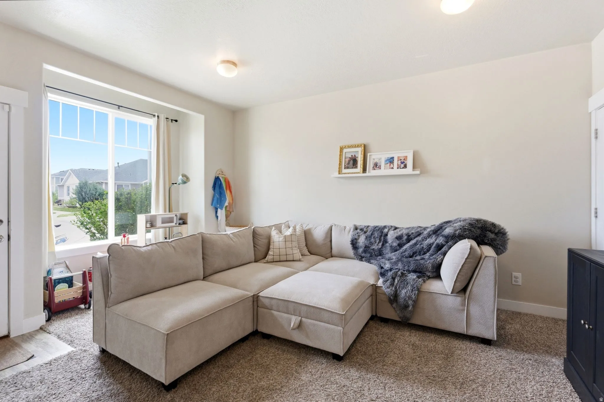 Bright living area featuring a large bay window, neutral-toned walls, and carpet flooring