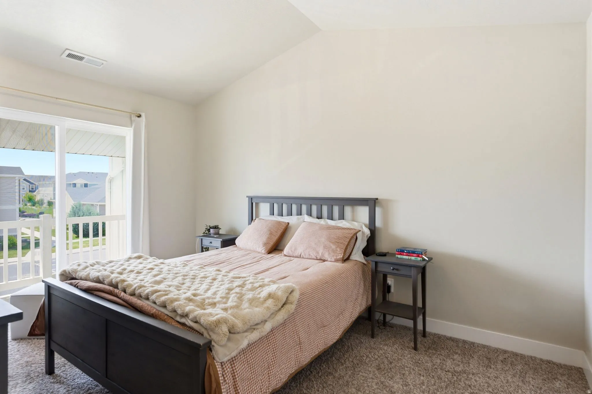 Carpeted bedroom featuring a vaulted ceiling and sliding glass doors opening to a balcony with white railings