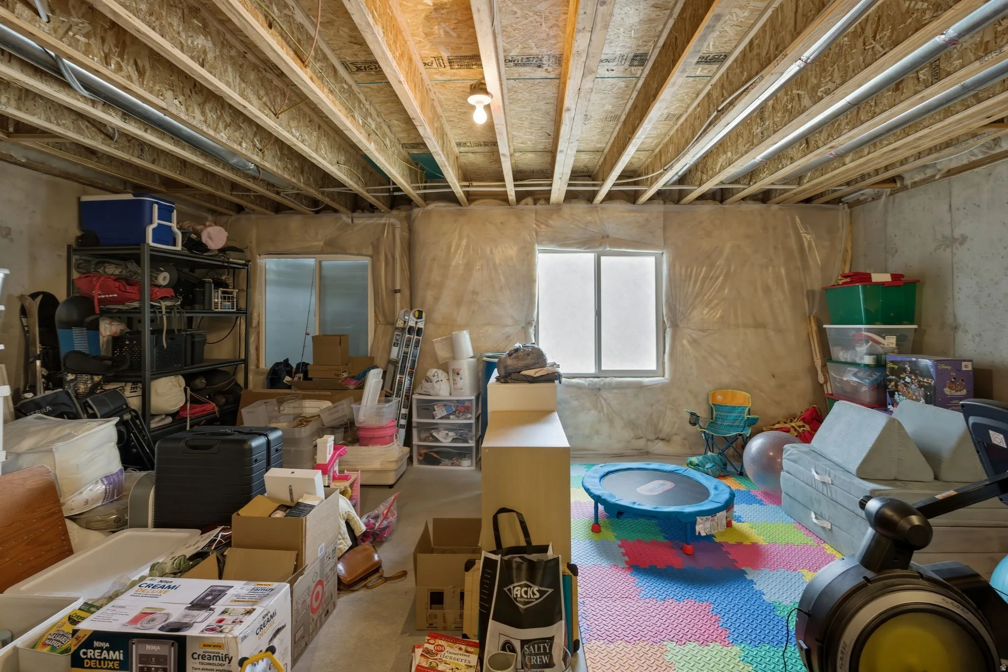 Unfinished basement featuring exposed wood joists and concrete walls, with two visible window wells providing natural light