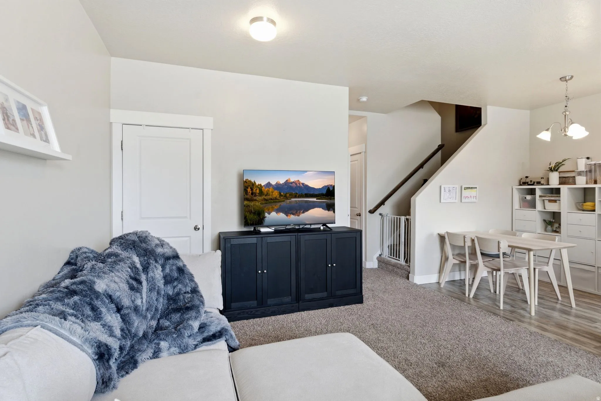 Open-concept living space with light-toned walls, recessed lighting, and a staircase featuring a dark wood handrail
