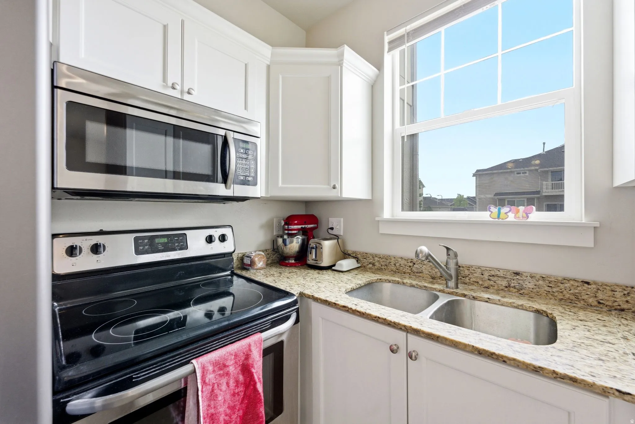 Bright kitchen featuring white cabinetry, granite-style countertops, and a stainless-steel double sink
