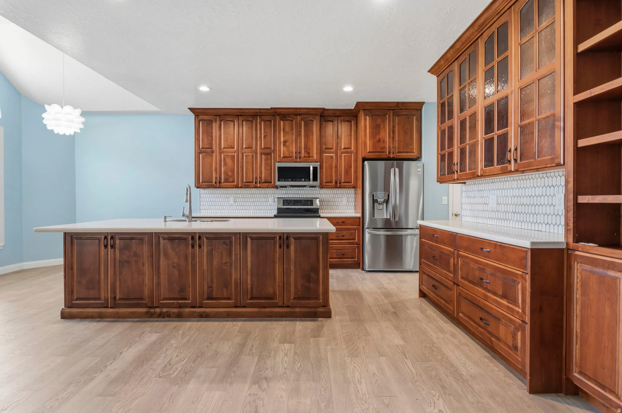 Kitchen featuring extensive wood cabinetry, a central island with a sink, white countertops, and a white picket tile backsplash
